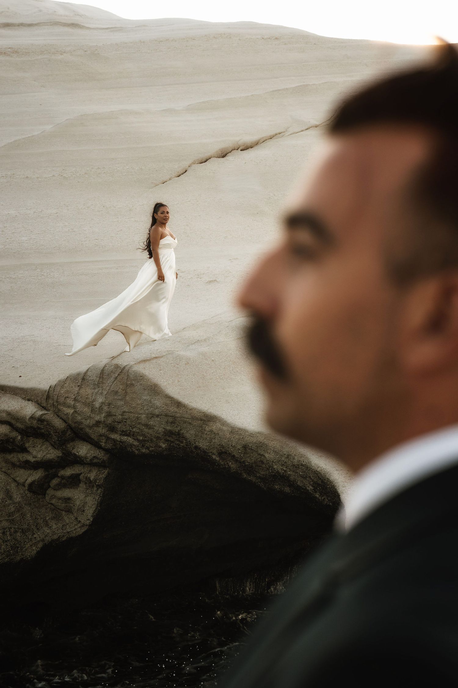 Dramatic desert wedding photoshoot with white dress contrasting against rocky landscape.