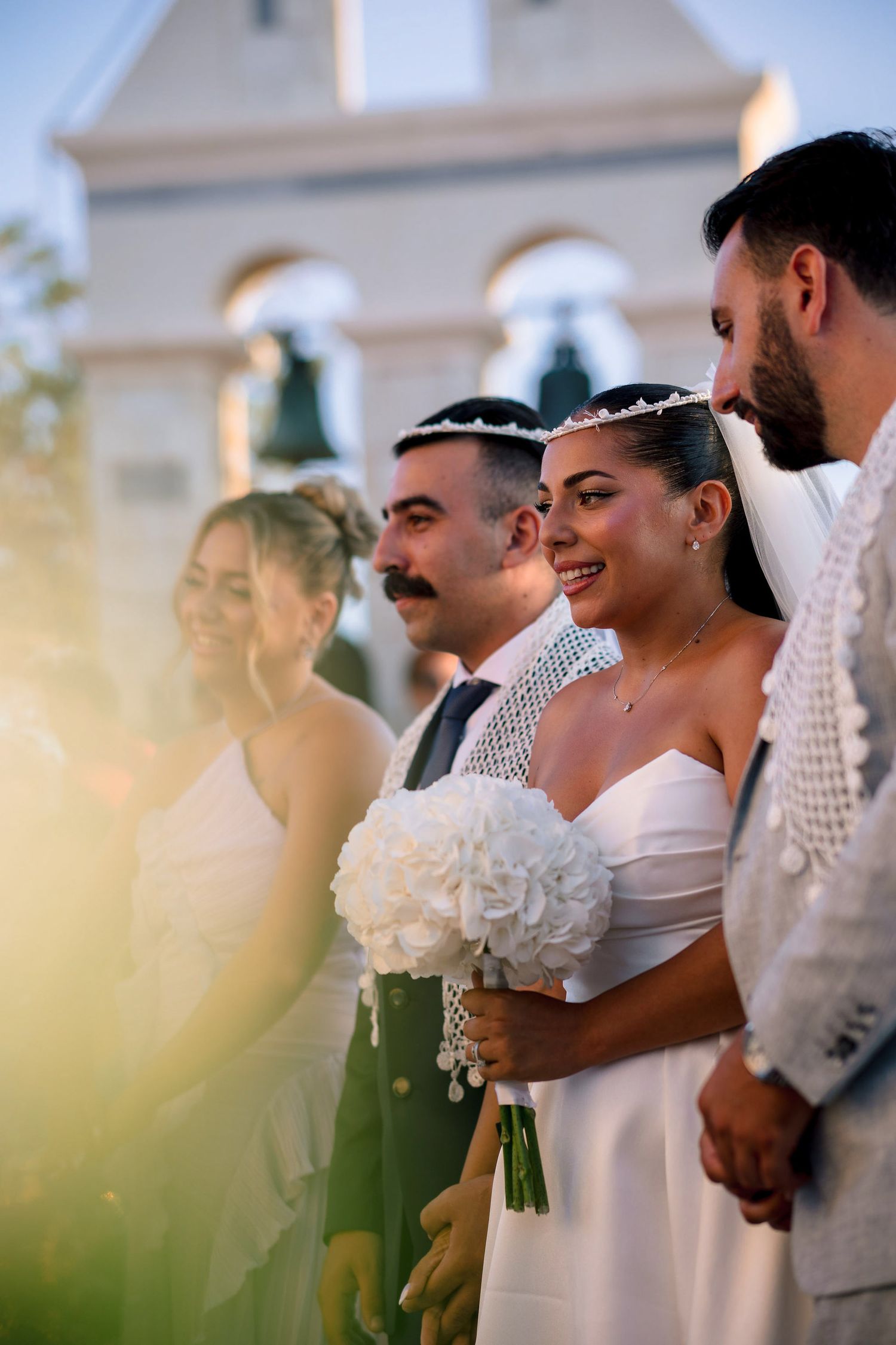Wedding ceremony group gathered outside a white church on a sunny day.