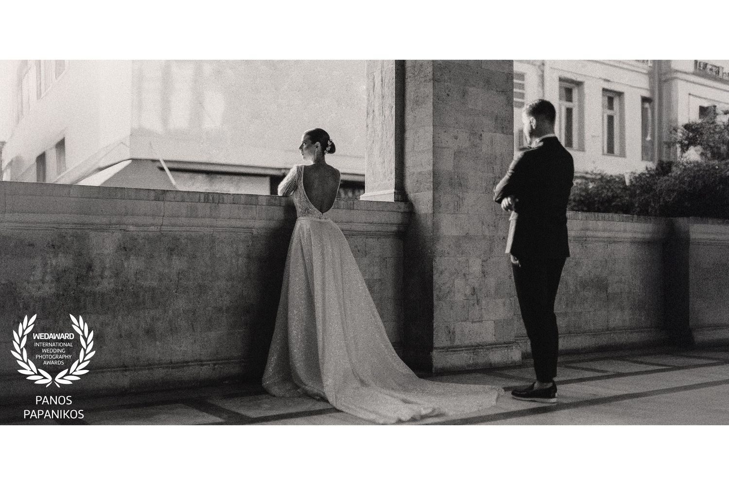 Black and white artistic wedding photo of couple standing separated by stone wall outdoors.