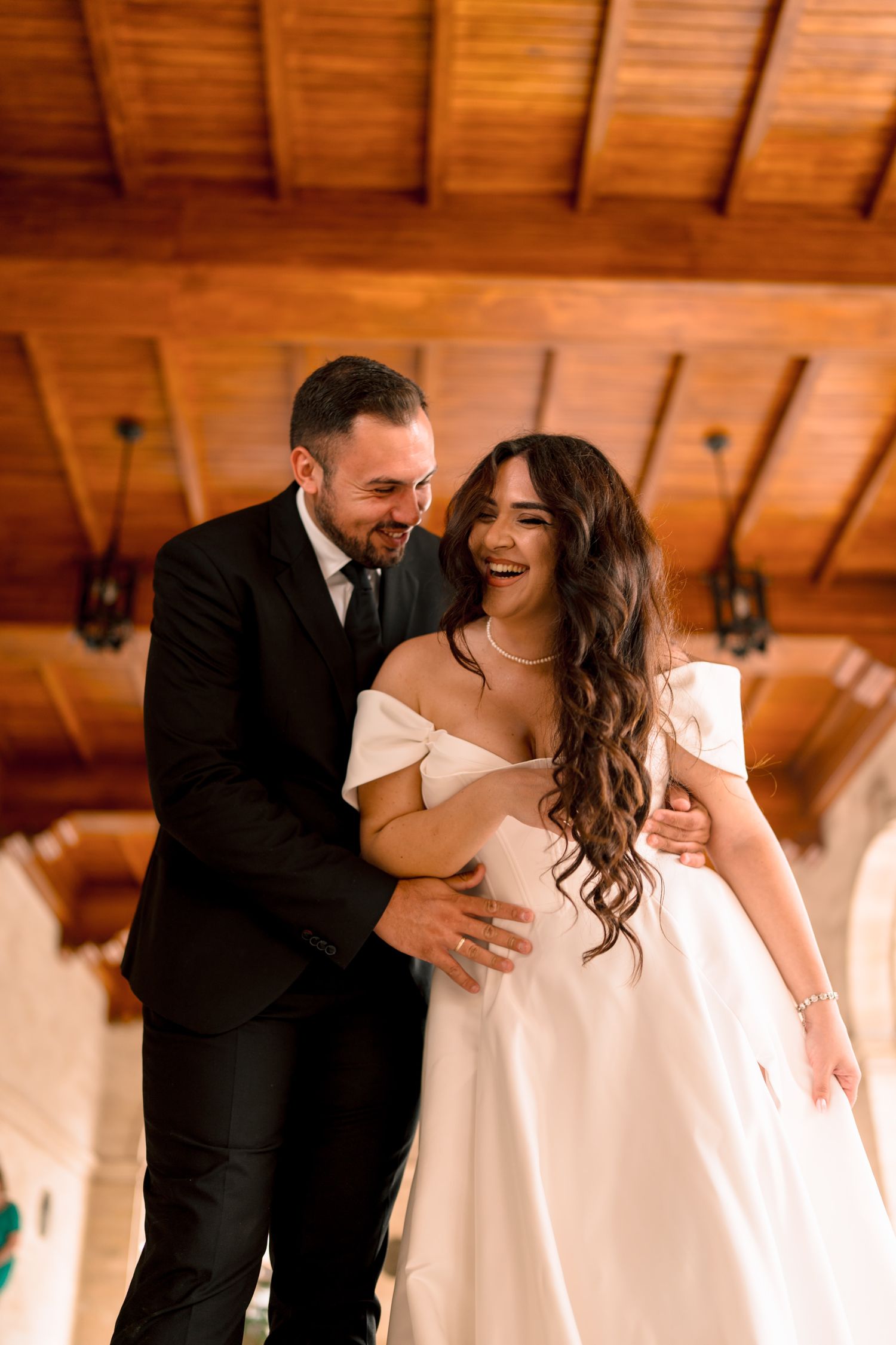 A romantic moment captured under warm wooden beams at a wedding venue.
