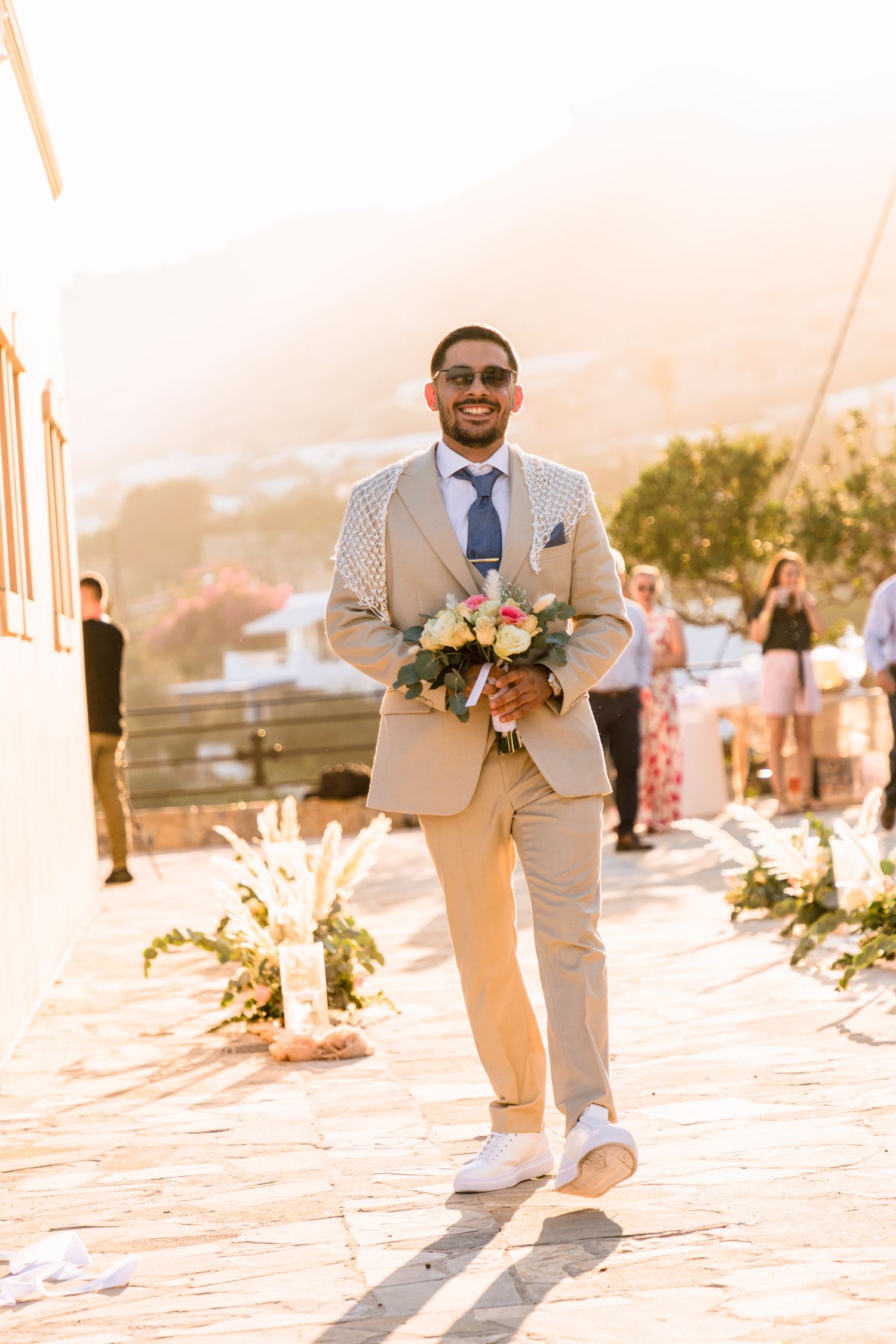 Wedding party member walking with floral bouquet during golden hour outdoor celebration.