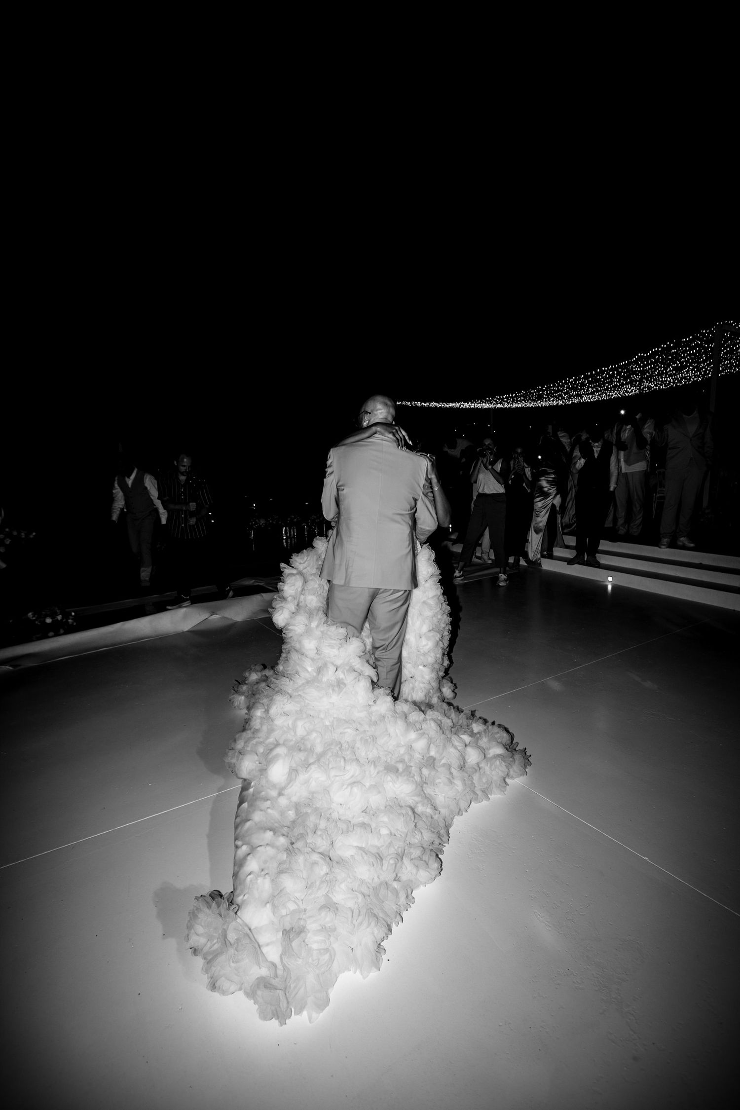 A black and white photo of a flowing wedding dress trailing across a dance floor.