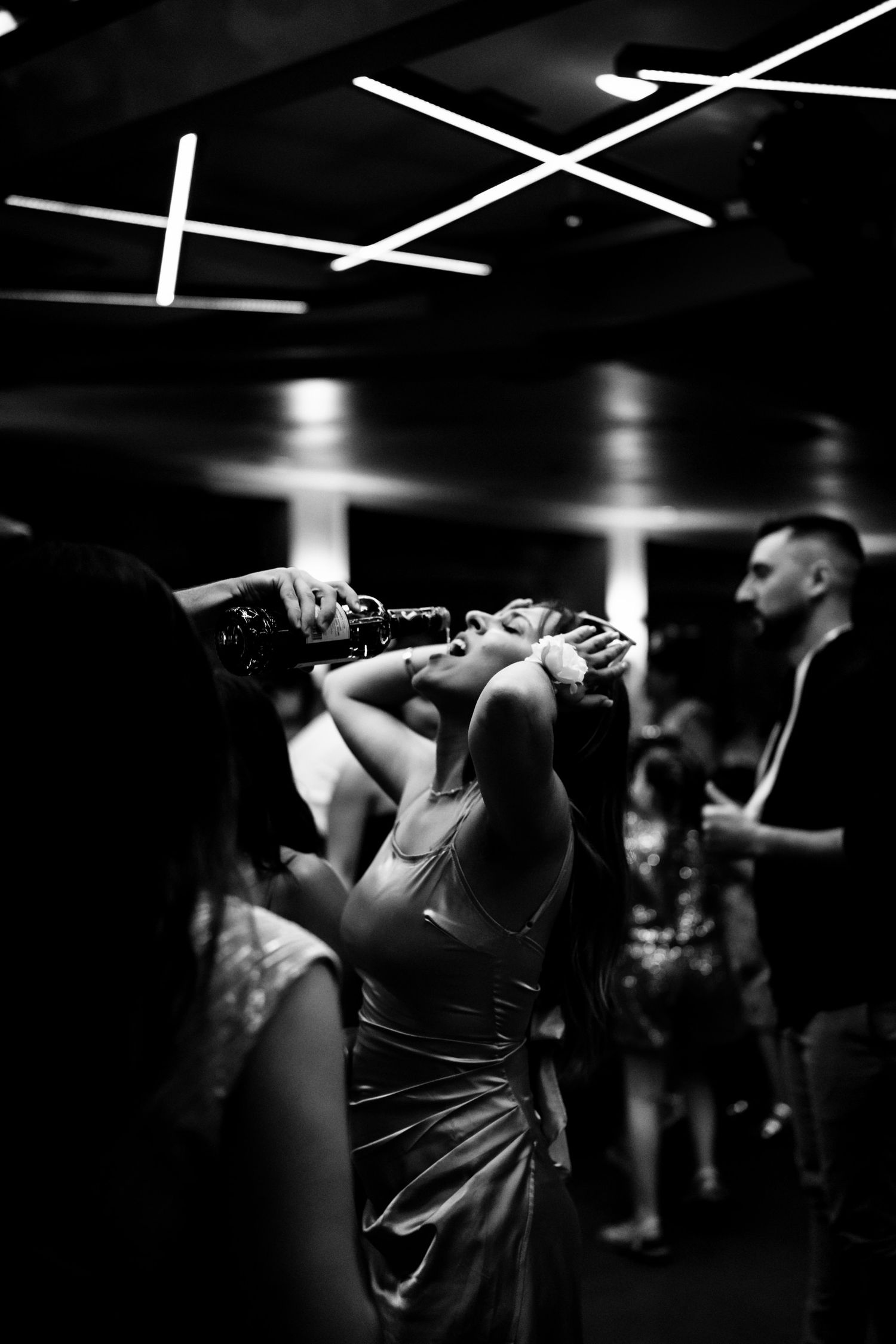 Dramatic black and white shot of guests dancing under geometric ceiling lights.
