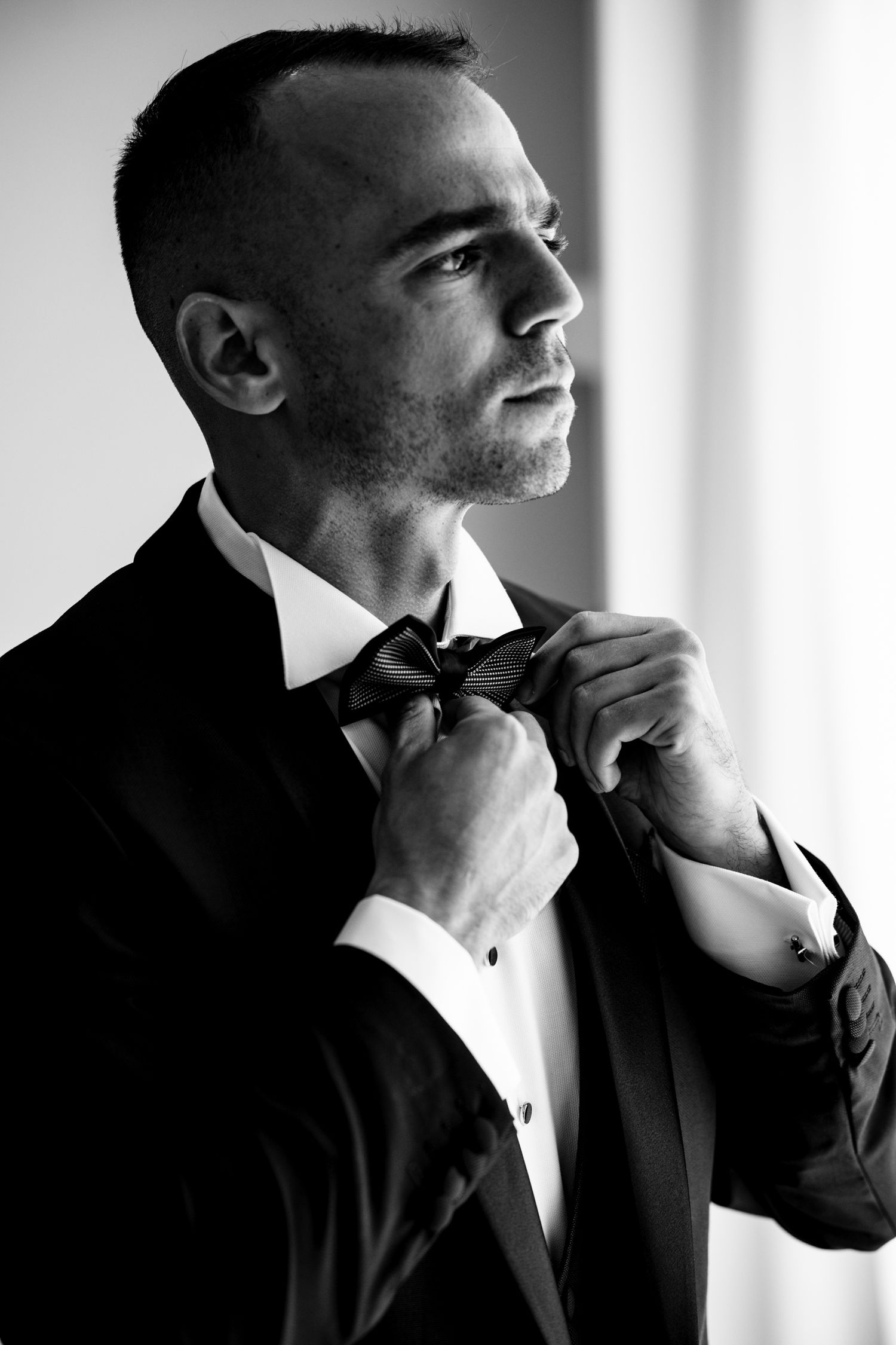 Black and white portrait series showing a groom adjusting his bow tie before the ceremony.