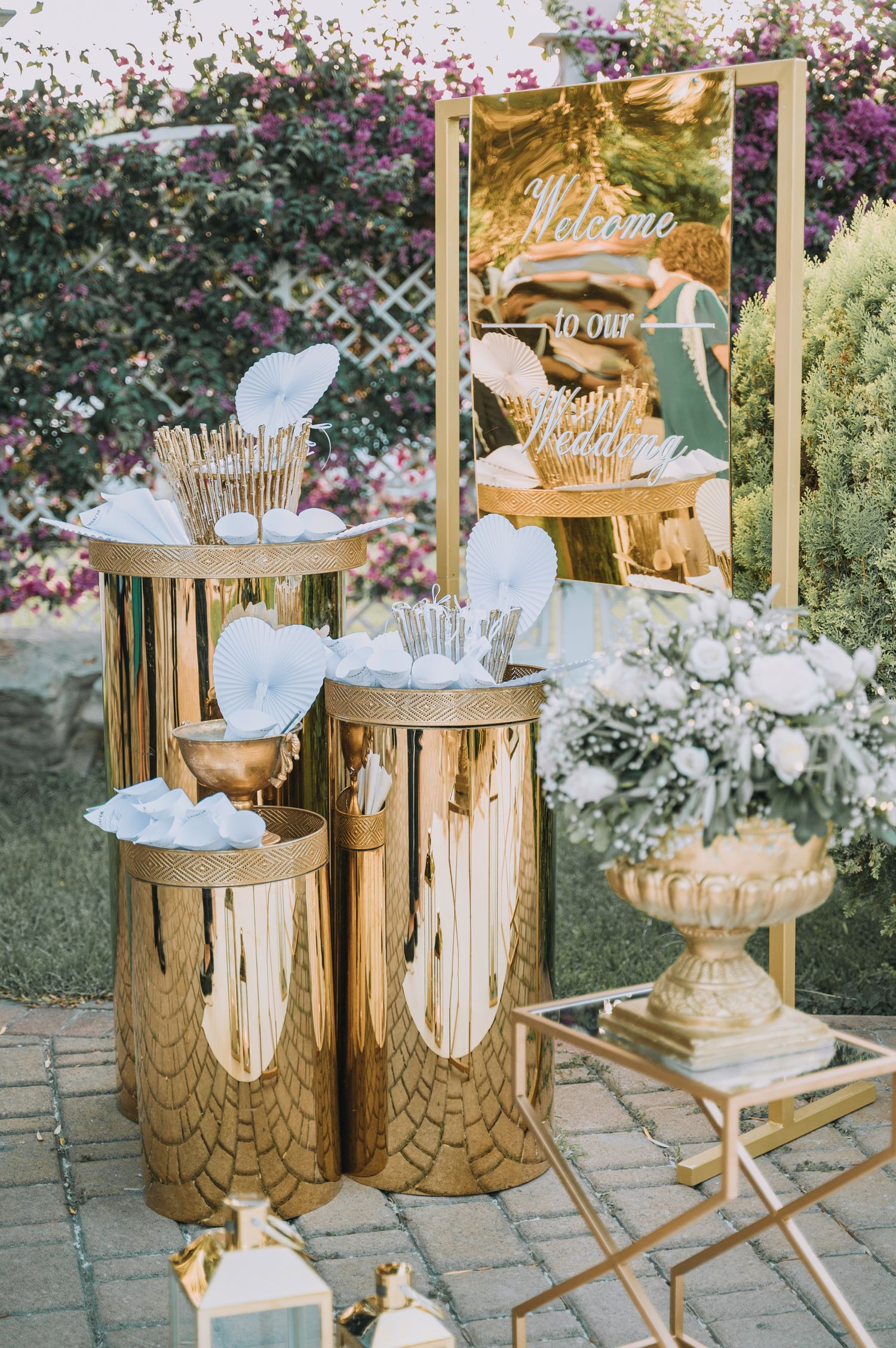 Elegant gold wedding decor display with metallic pedestals and white accents in a garden setting.
