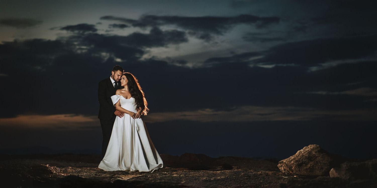 Wedding couple poses against moody twilight sky on rocky terrain.