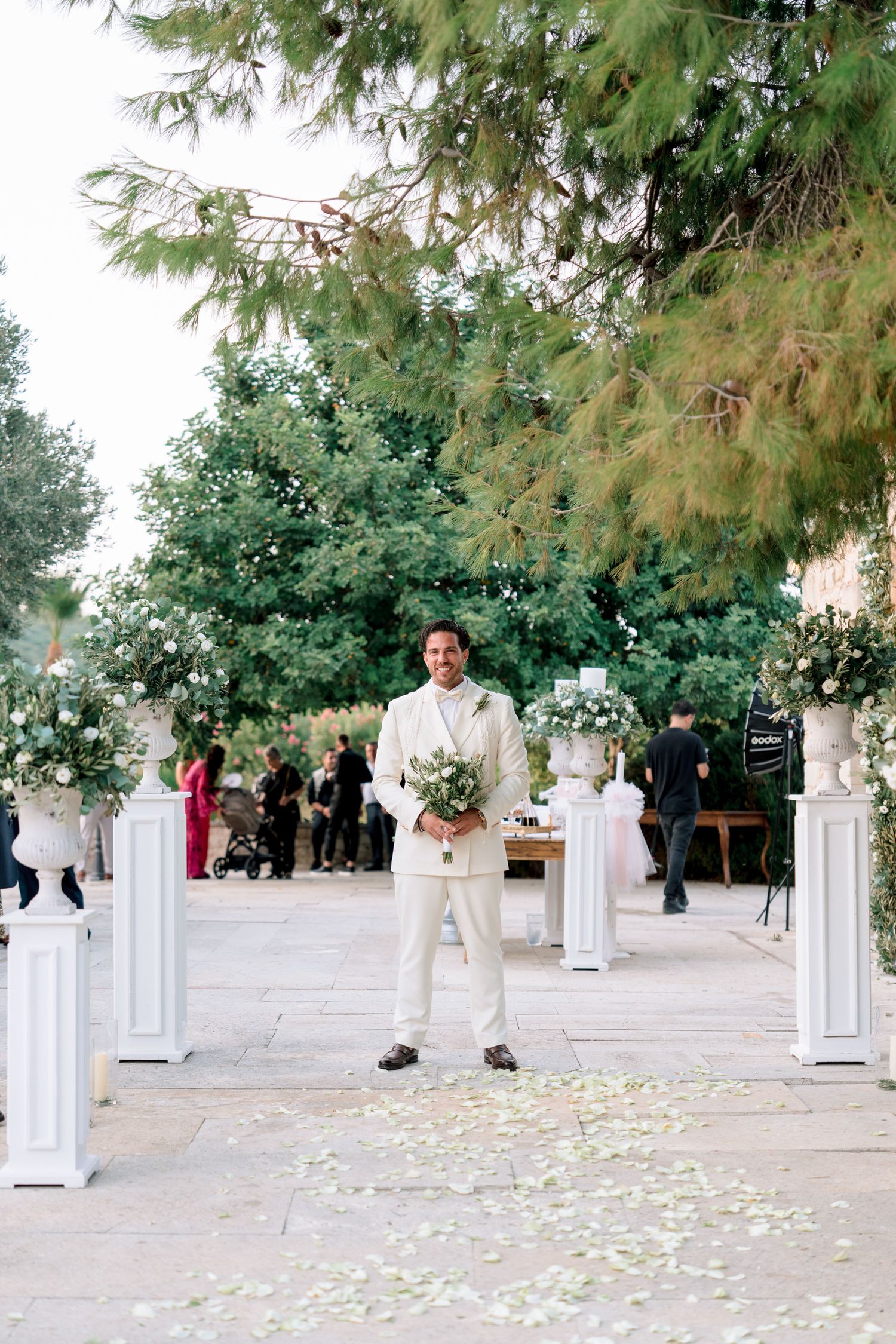 A wedding ceremony setup with white pillars and flower petals scattered on the ground.