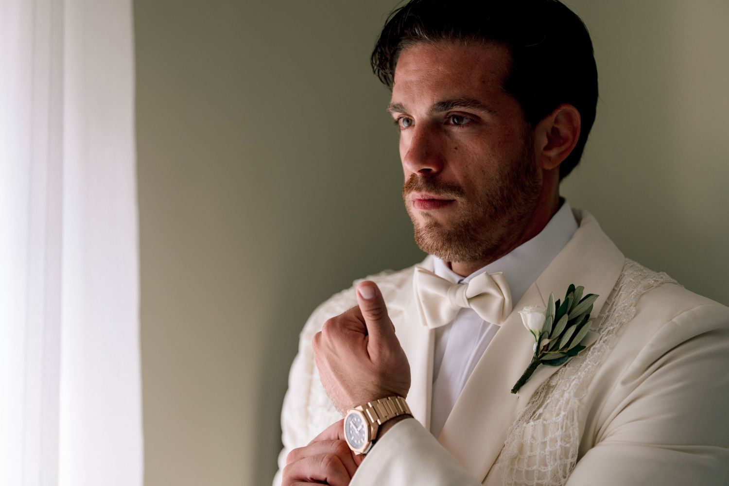 People in white formal attire gathered together, with one wearing a small green boutonniere.