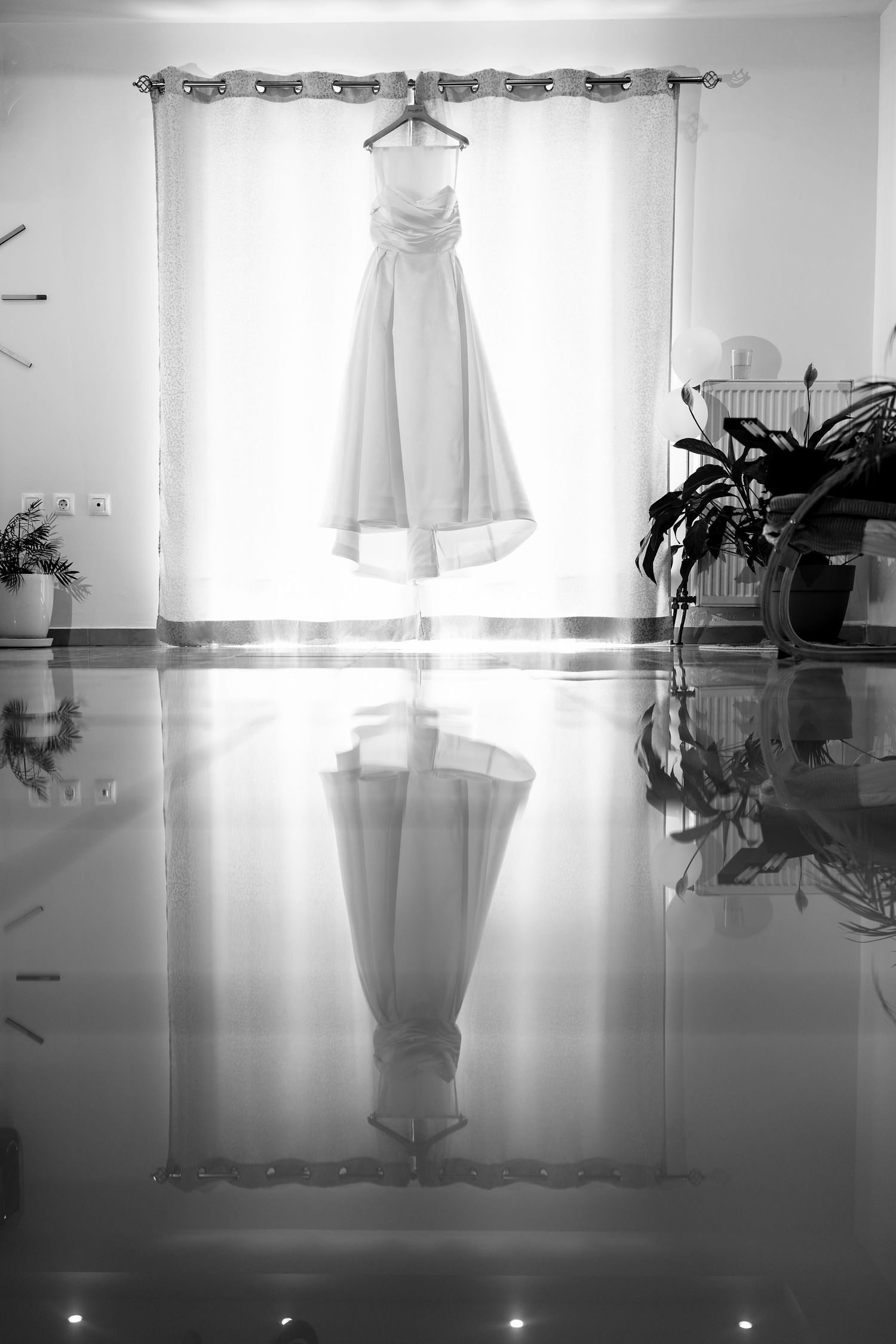 Wedding dress hanging in front of bright window creating silhouette effect.