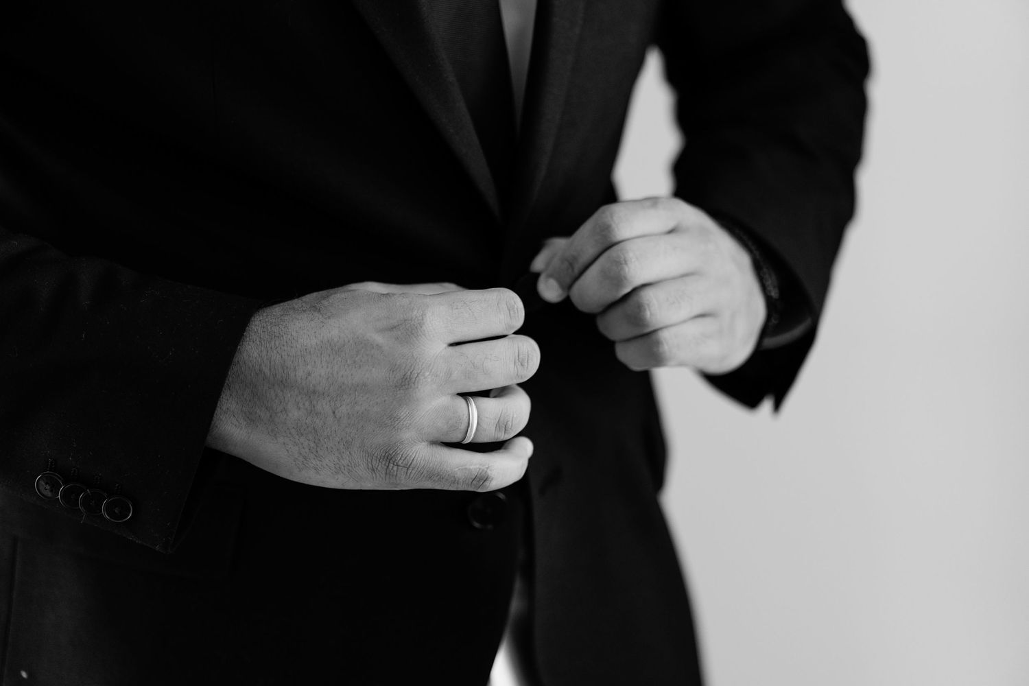 Close-up of hands adjusting formal black suit cuffs and buttons.
