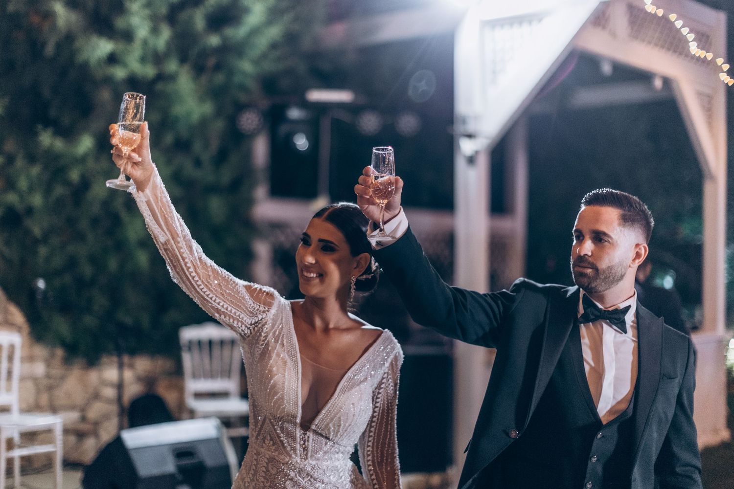 Wedding guests toasting with champagne glasses during an outdoor evening celebration.