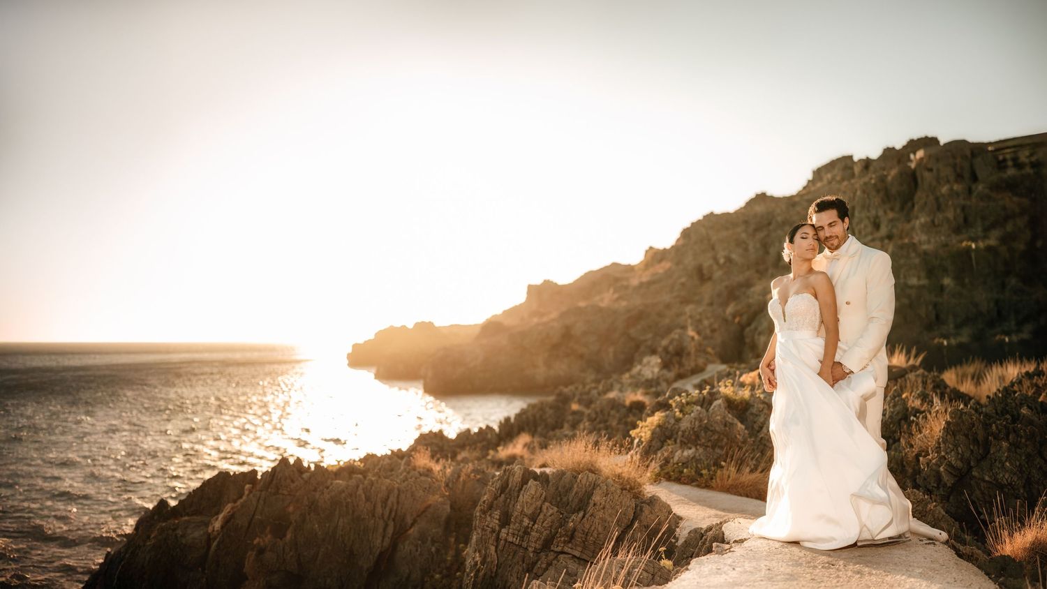 A panoramic coastal wedding scene with cliffs and ocean at golden hour.