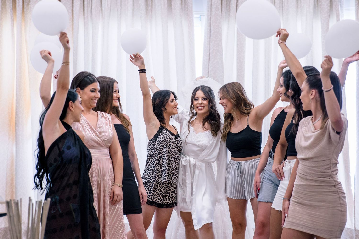 People dancing and celebrating in a bright room with white curtains.