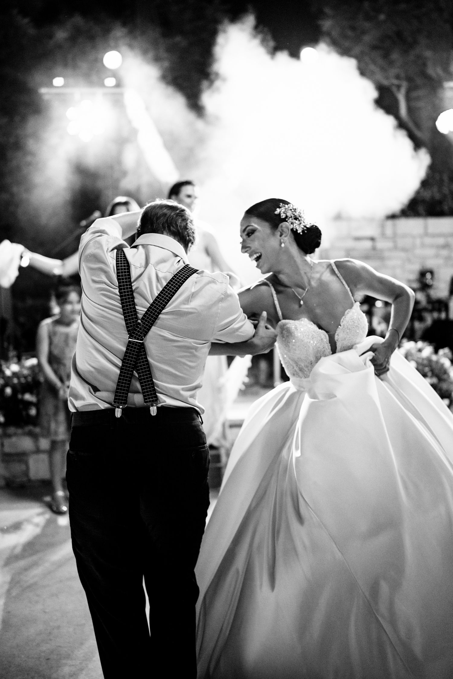 Black and white capture of joyful dancing at wedding reception with atmospheric lighting.