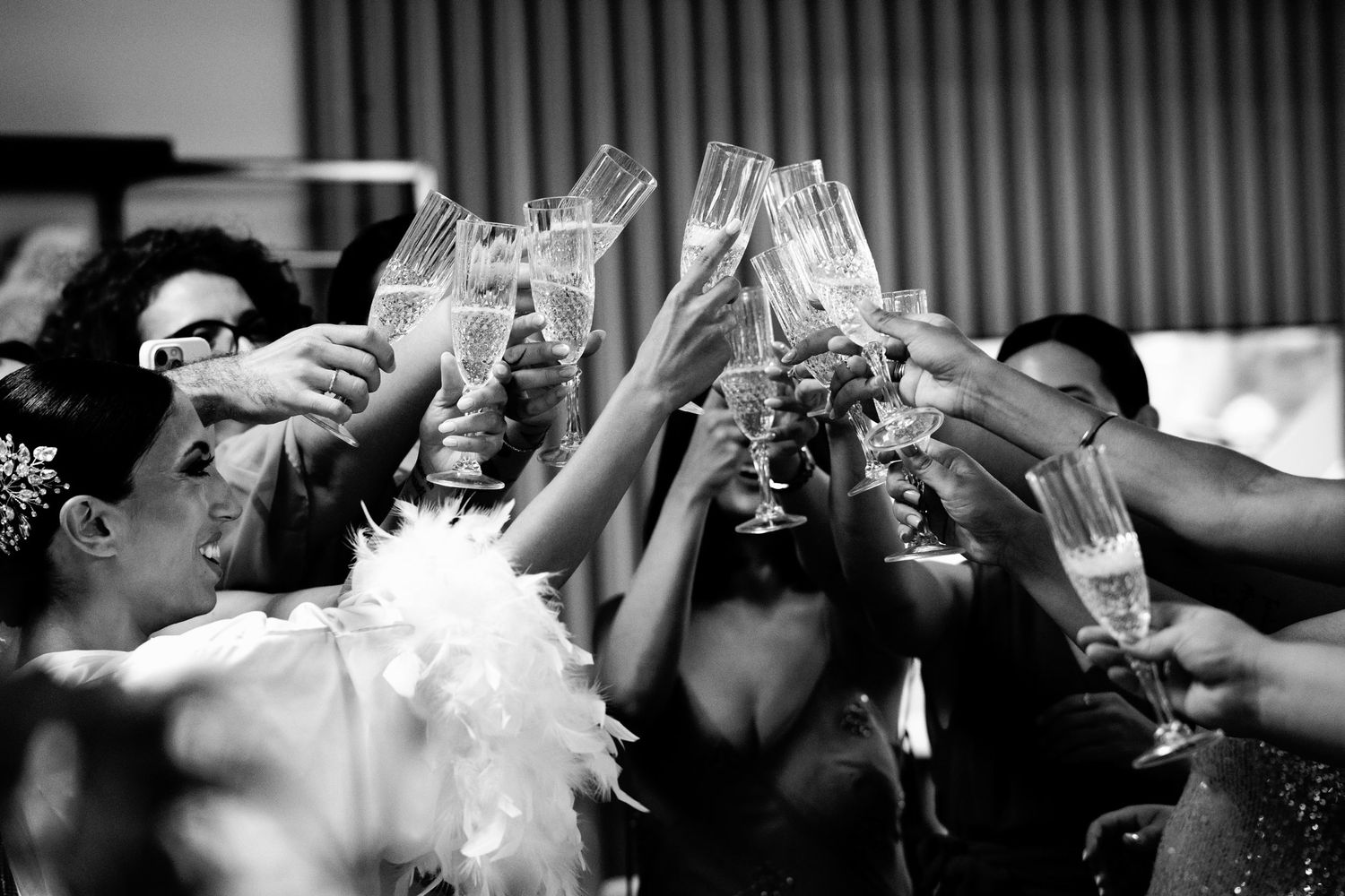 Black and white photo of wedding guests raising champagne glasses in celebration.