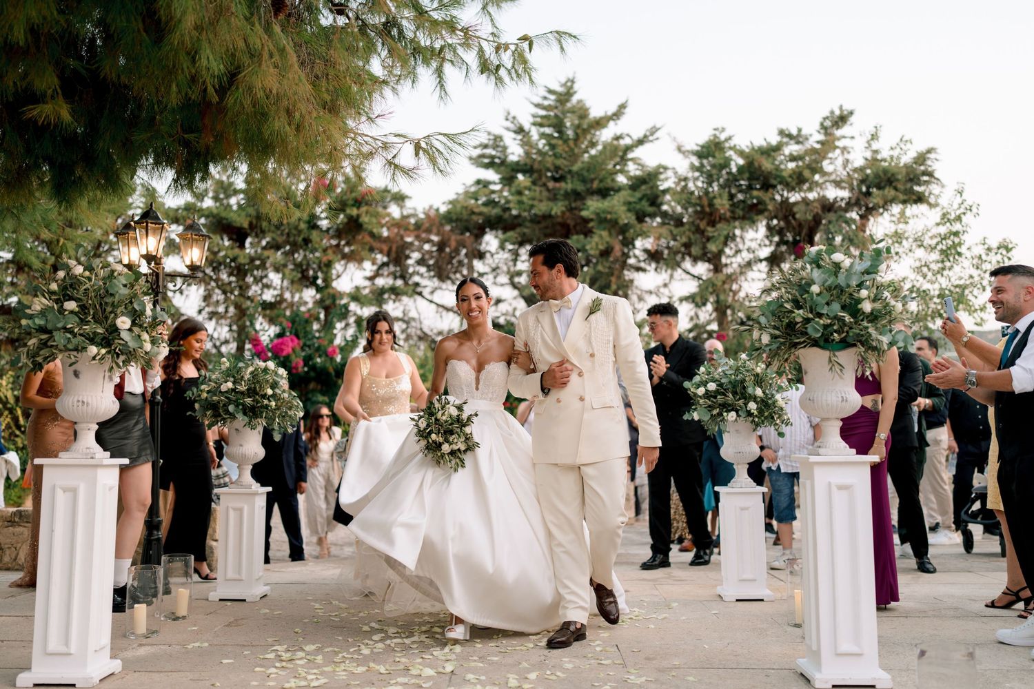 Wedding celebration with guests gathered on an outdoor garden path surrounded by trees.
