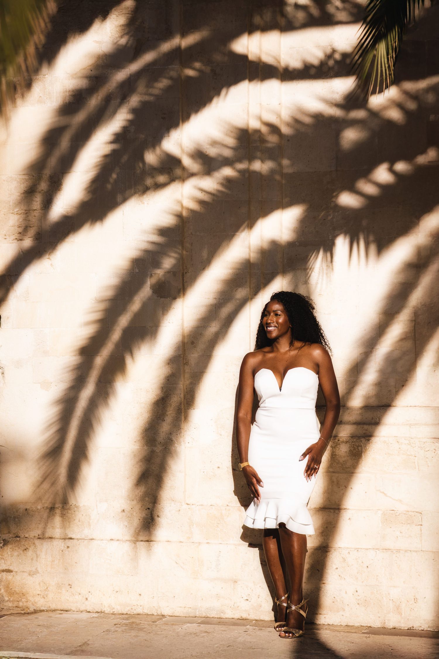 Artistic portrait against white wall with dramatic palm tree shadow patterns.