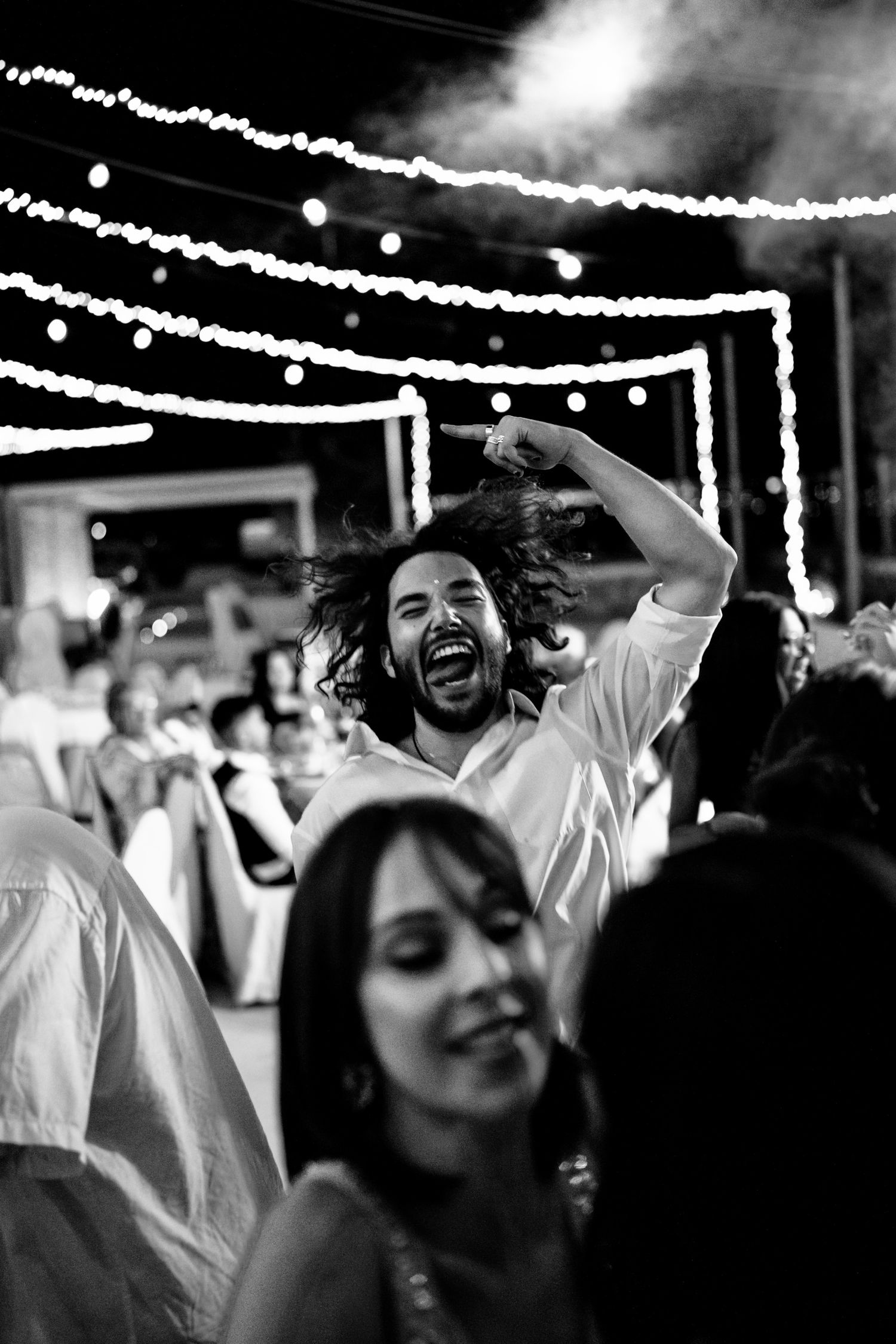 Black and white celebration photo with string lights overhead and joyful party atmosphere.