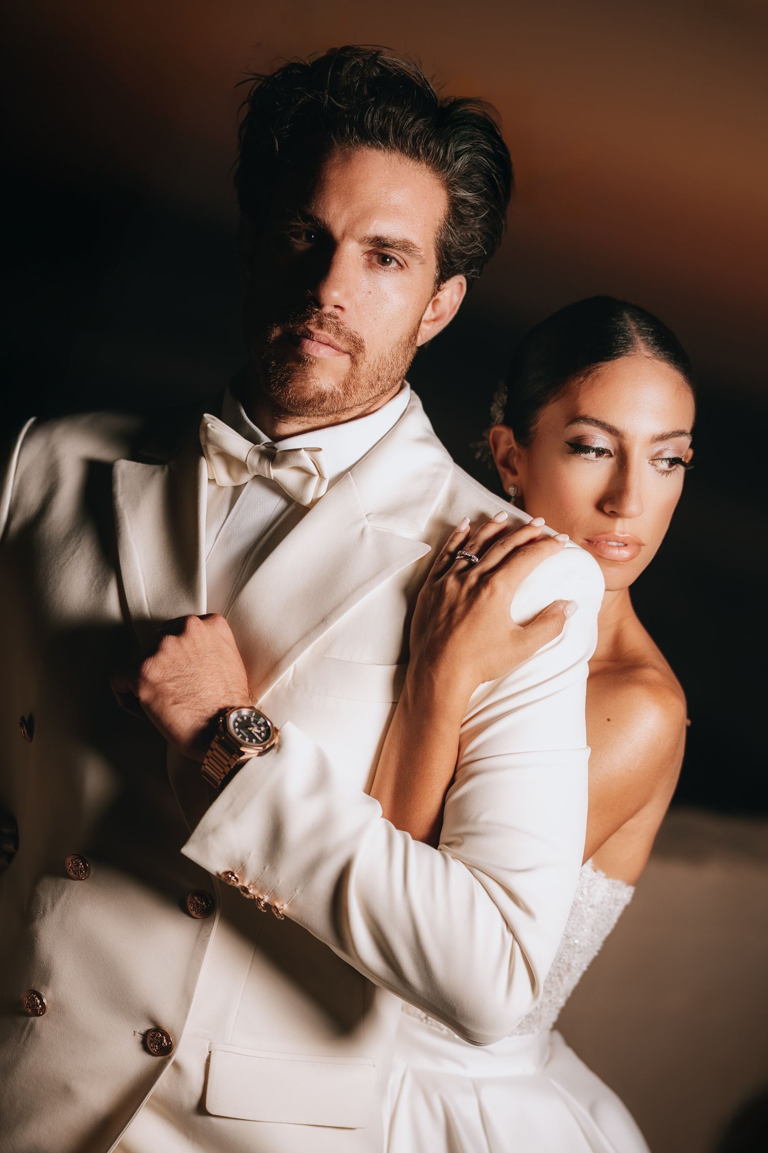 Romantic studio portraits of couple in white wedding attire against dark background.
