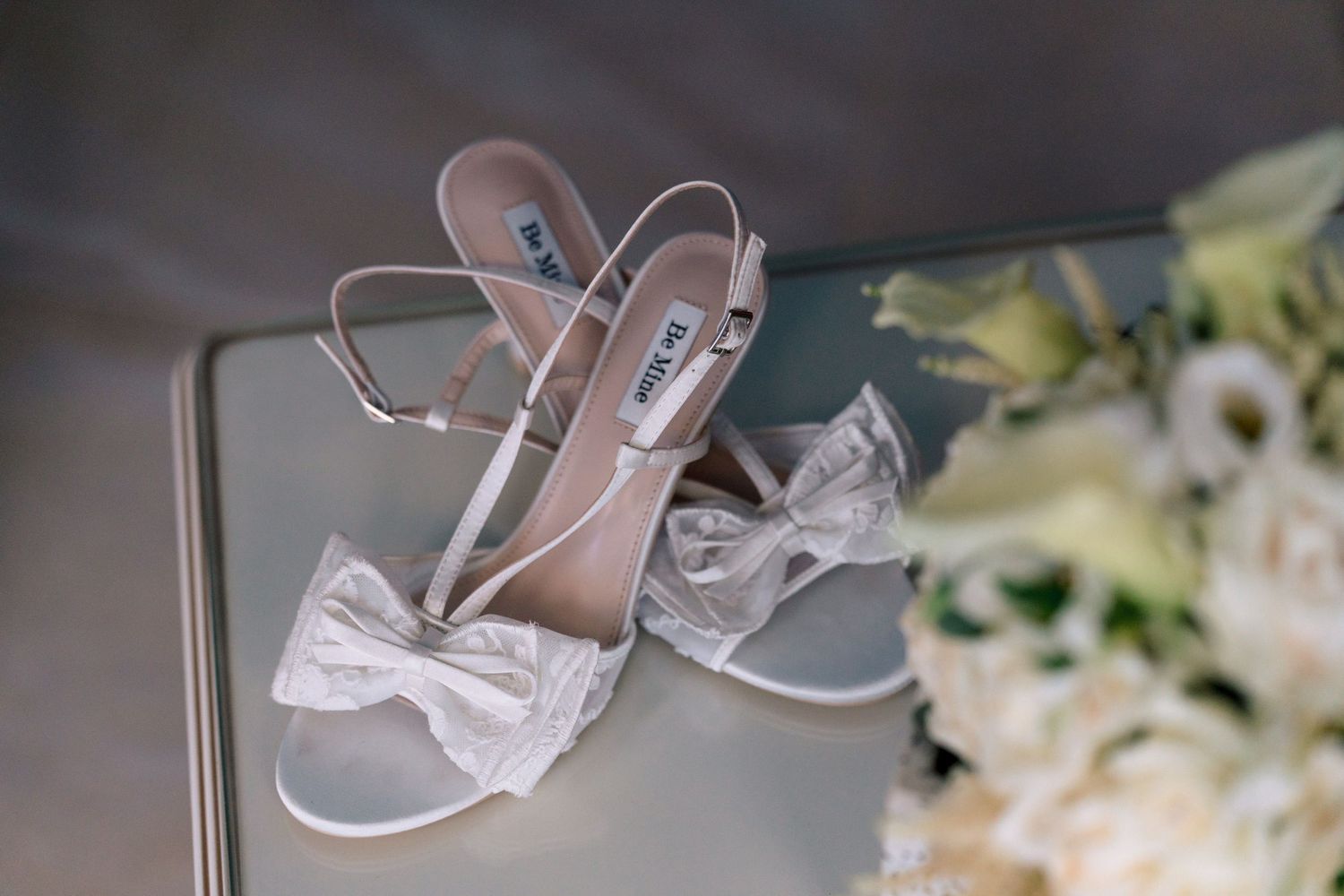 White lace bridal shoes displayed with floral arrangements.