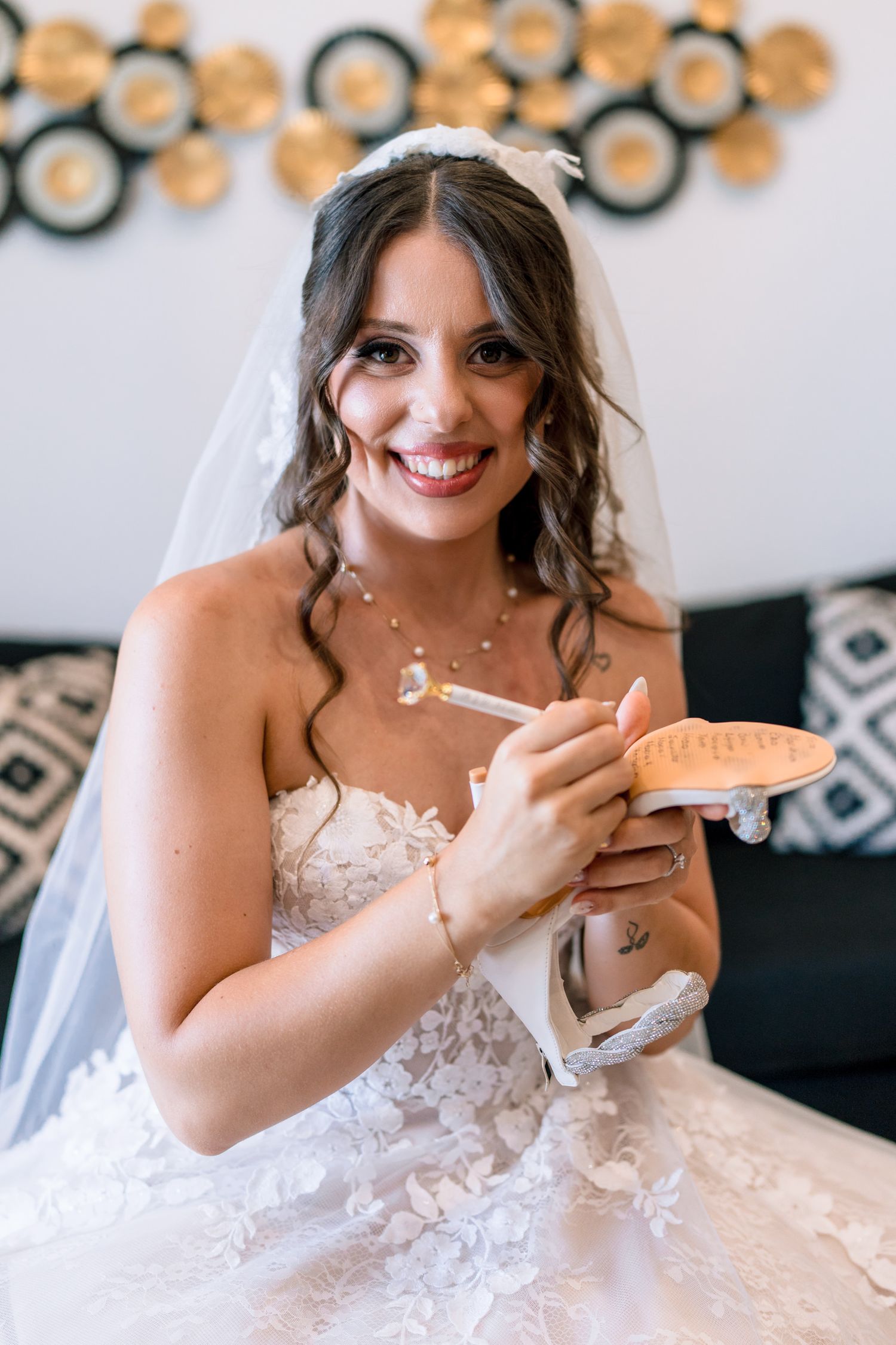 Bride in white lace dress sitting on couch with decorative gold circles on wall behind.