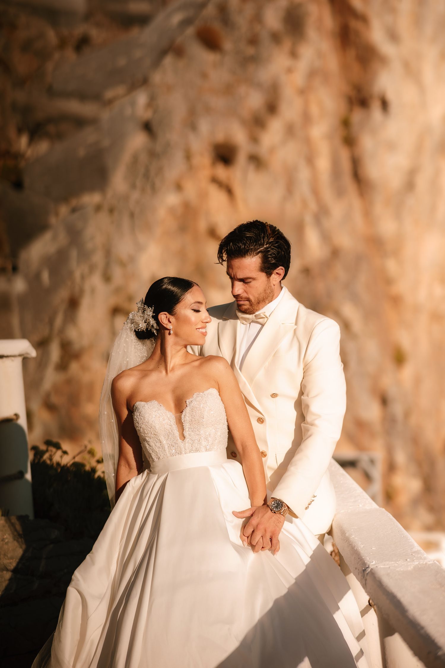 Couple in white wedding attire share intimate moments against rocky backdrop.