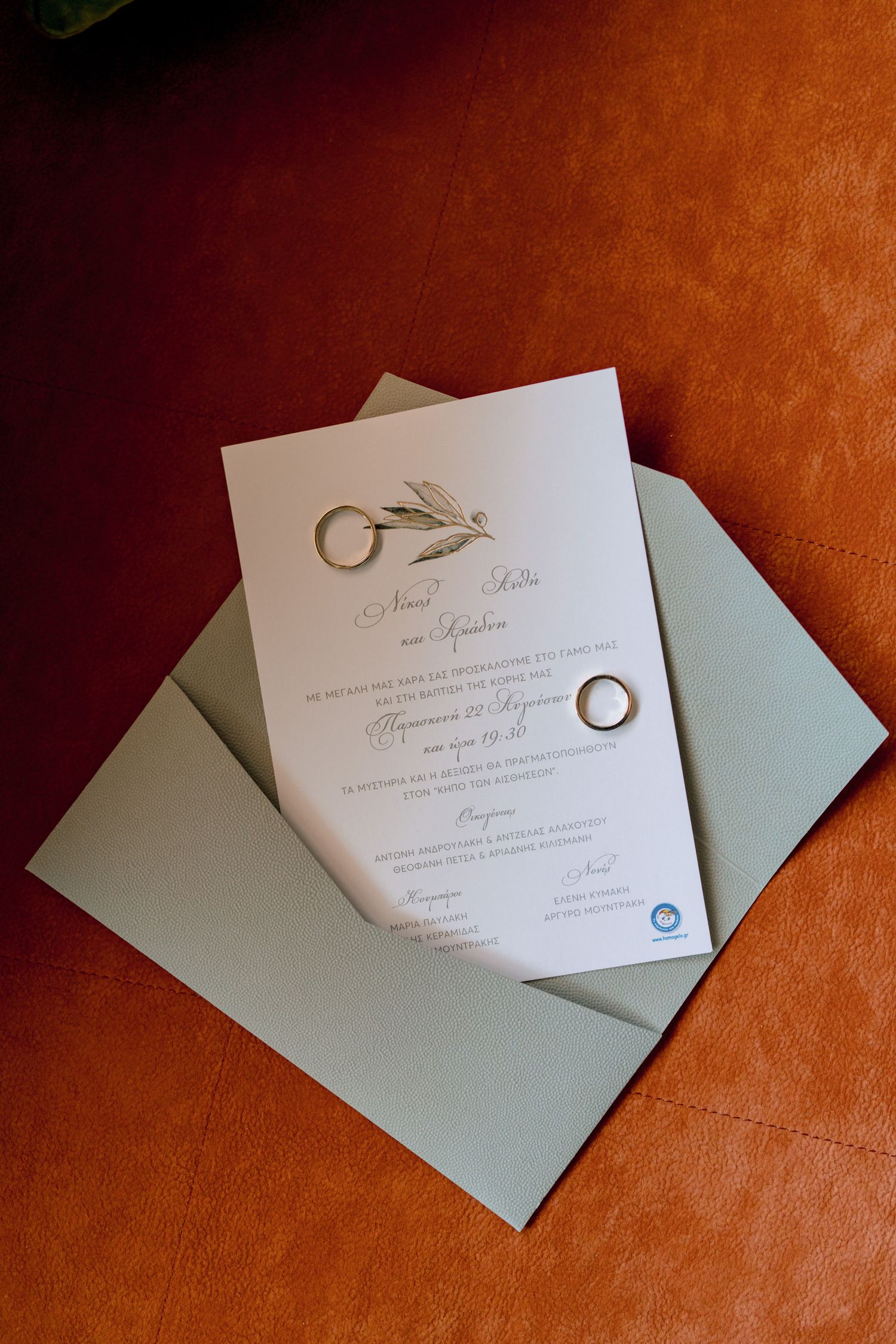 Wedding invitation and rings displayed on brown leather surface with mint green envelope.