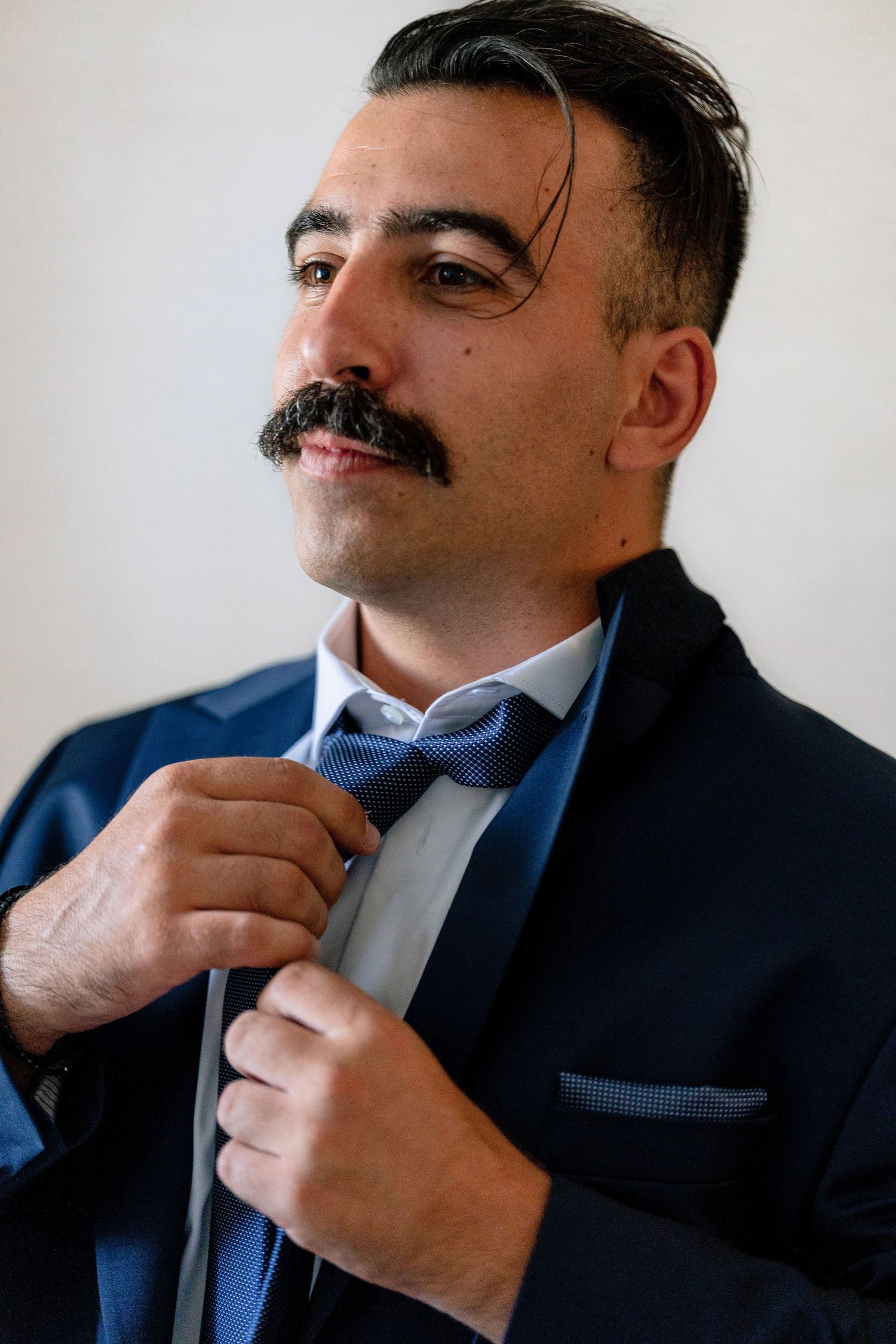Close-up sequence of adjusting a bow tie and collar on a navy suit.