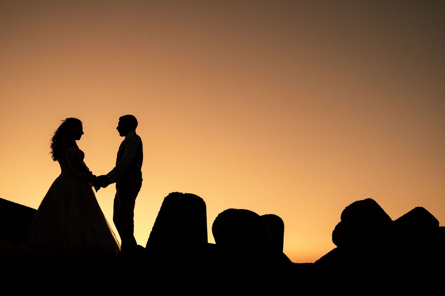 Silhouettes of figures against a warm sunset sky create a romantic mood.