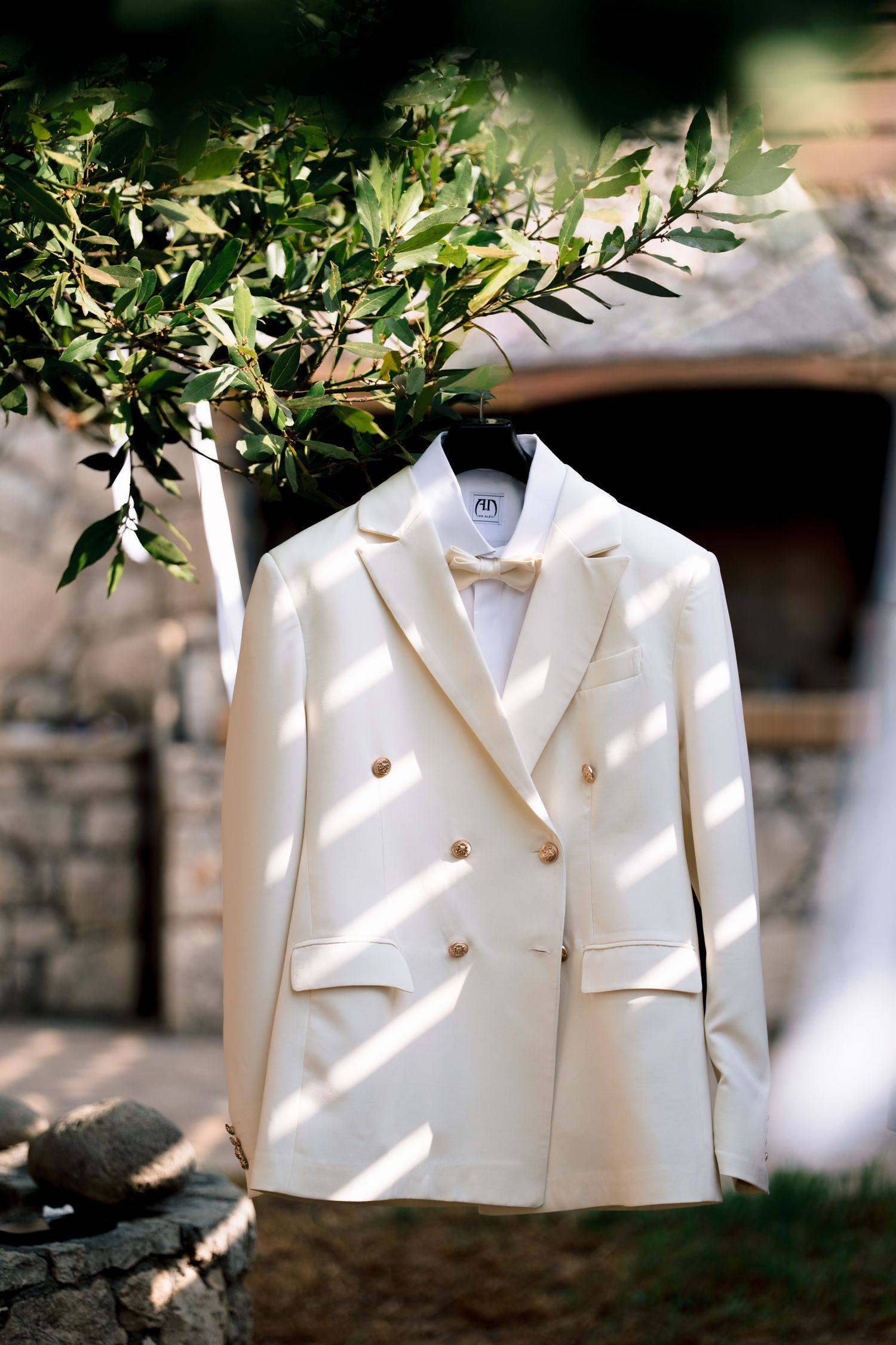 White formal jacket hanging outdoors against greenery and natural lighting.