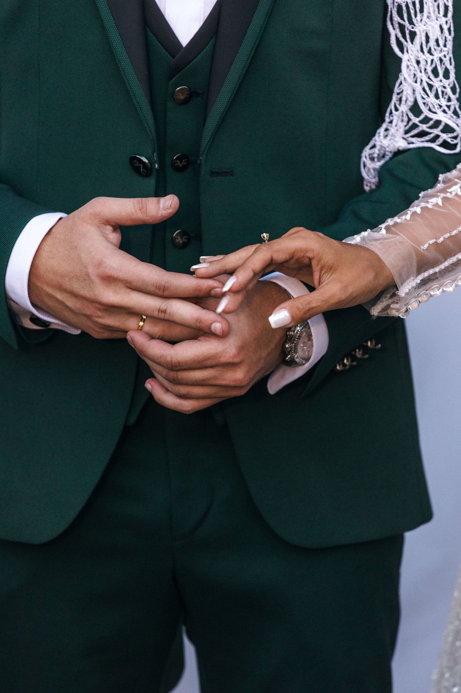 Close-up of hands during ring exchange with emerald green suit jacket visible.
