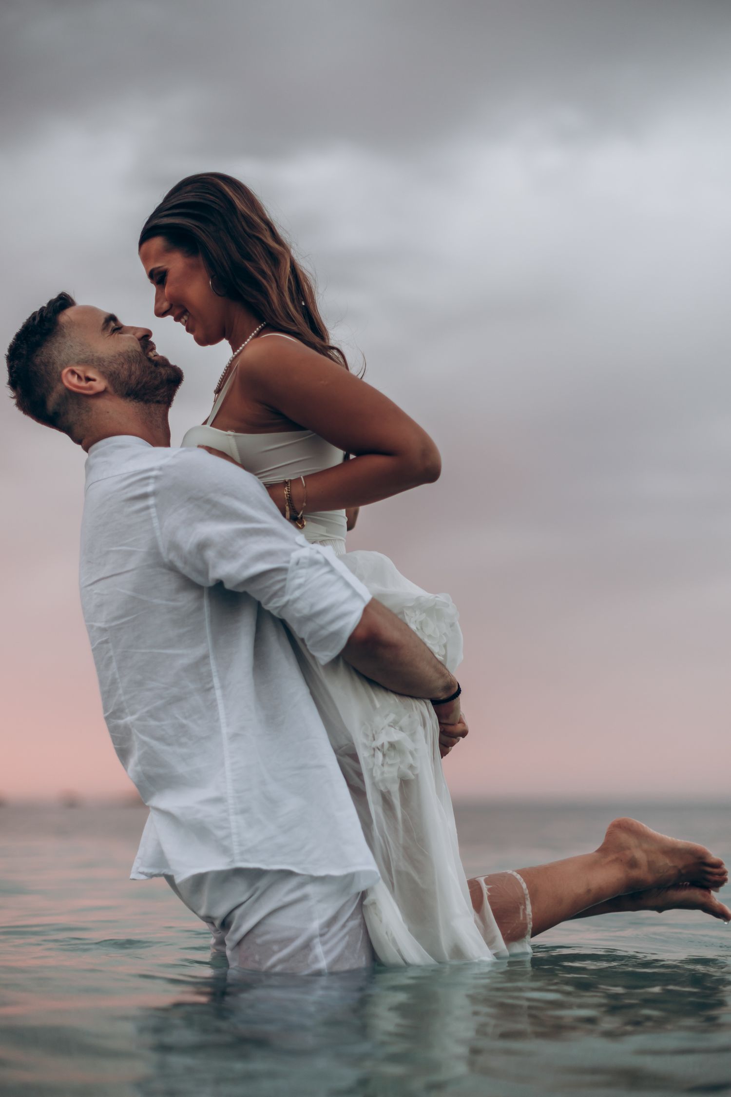 Playful couple splashes in ocean water during golden hour photo session.