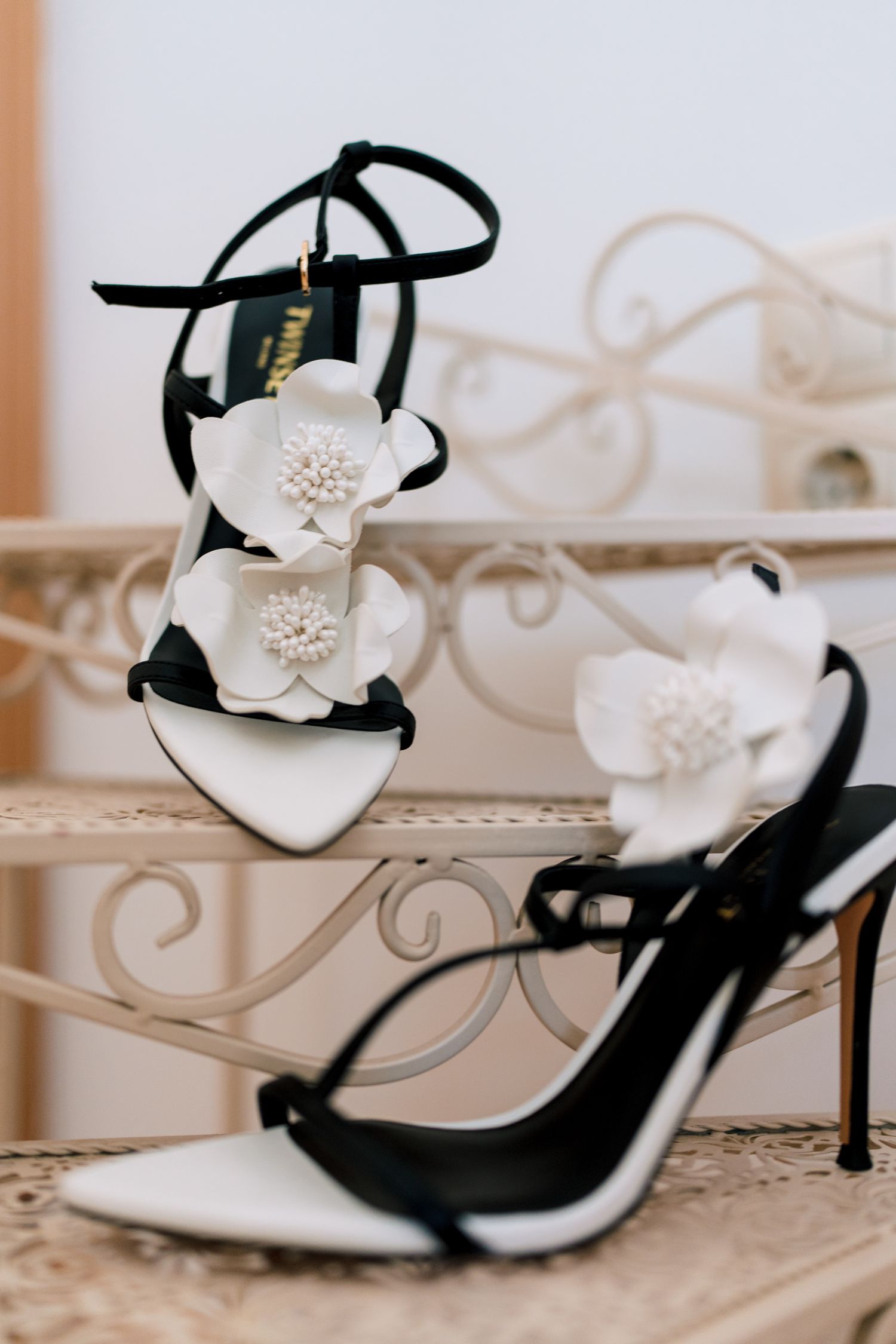 Elegant white bridal shoes with pearl embellishments and black straps on a textured surface.