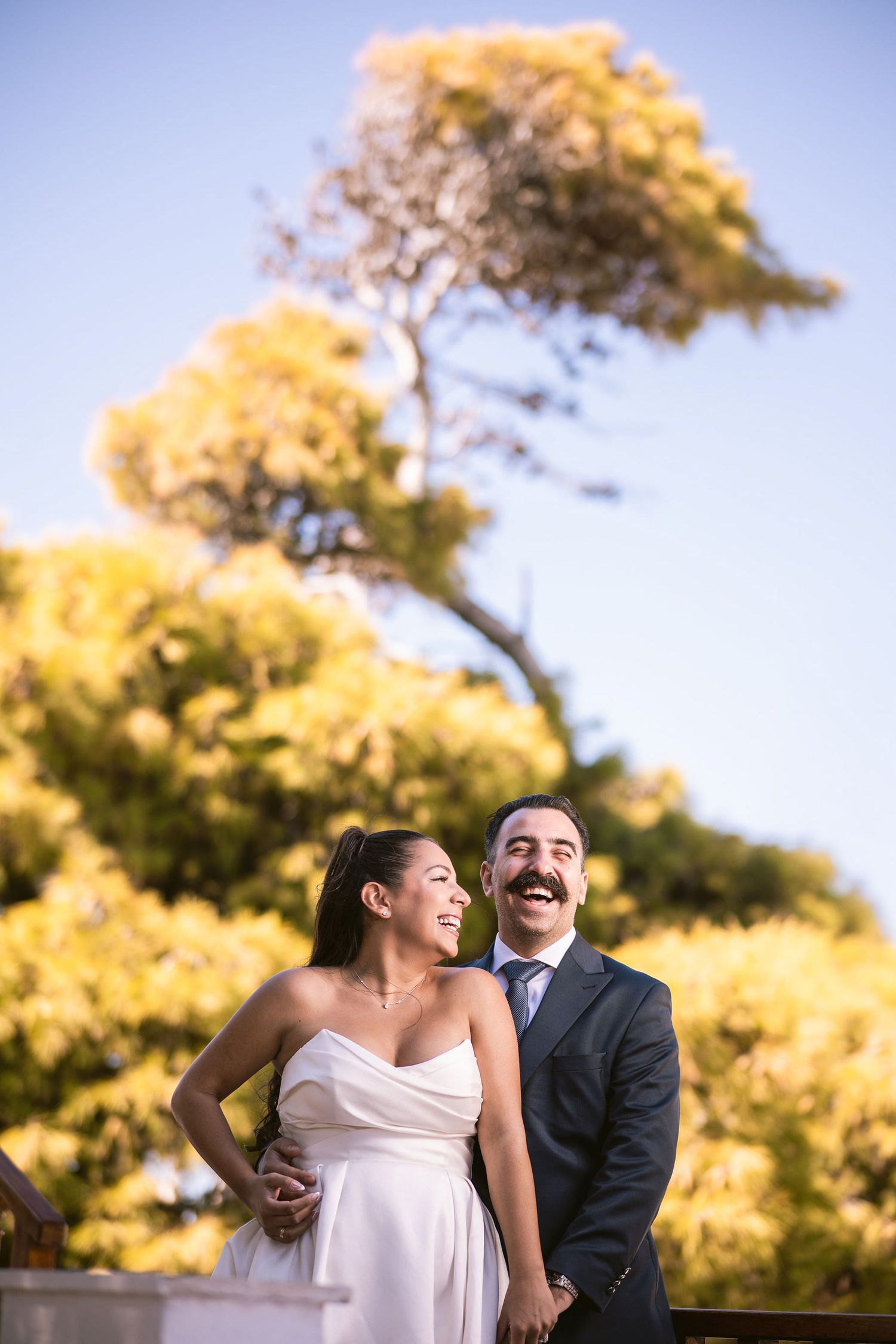 Joyful wedding couple laughing together beneath autumn foliage.