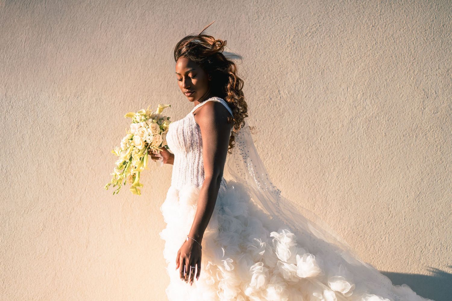 Artistic bridal portrait against textured wall with dramatic lighting.