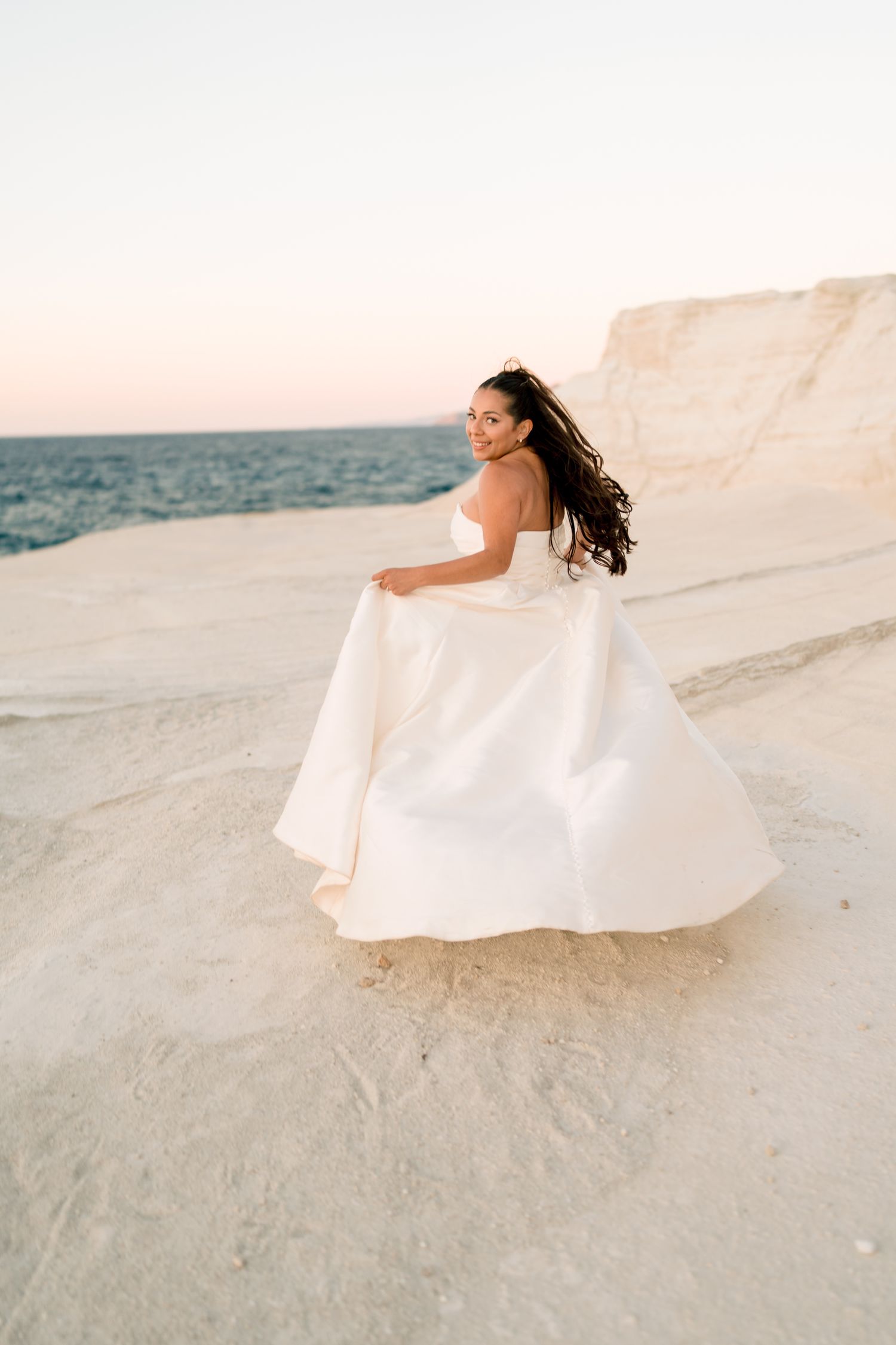 Wedding dress billowing in the wind against white coastal cliffs at sunset.