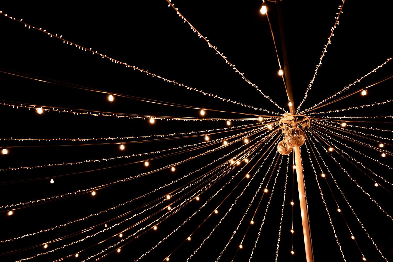 String lights form a starburst pattern against dark night sky at outdoor event.