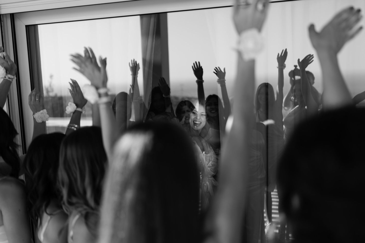 Silhouettes of raised hands celebrating against a bright window.