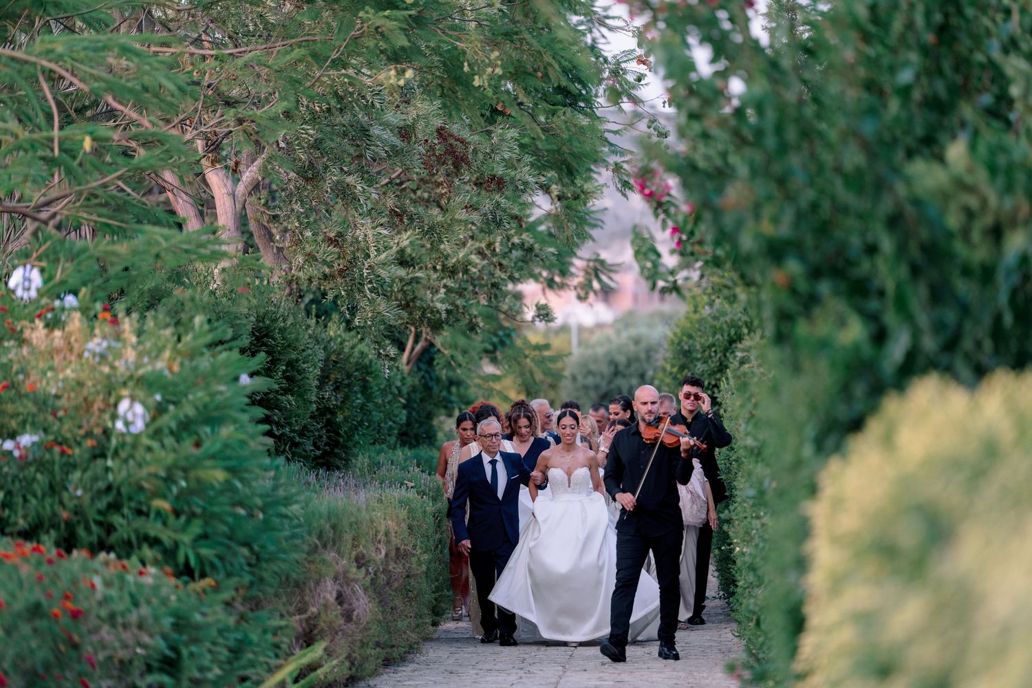 Wedding celebration procession walking through a lush green garden pathway.