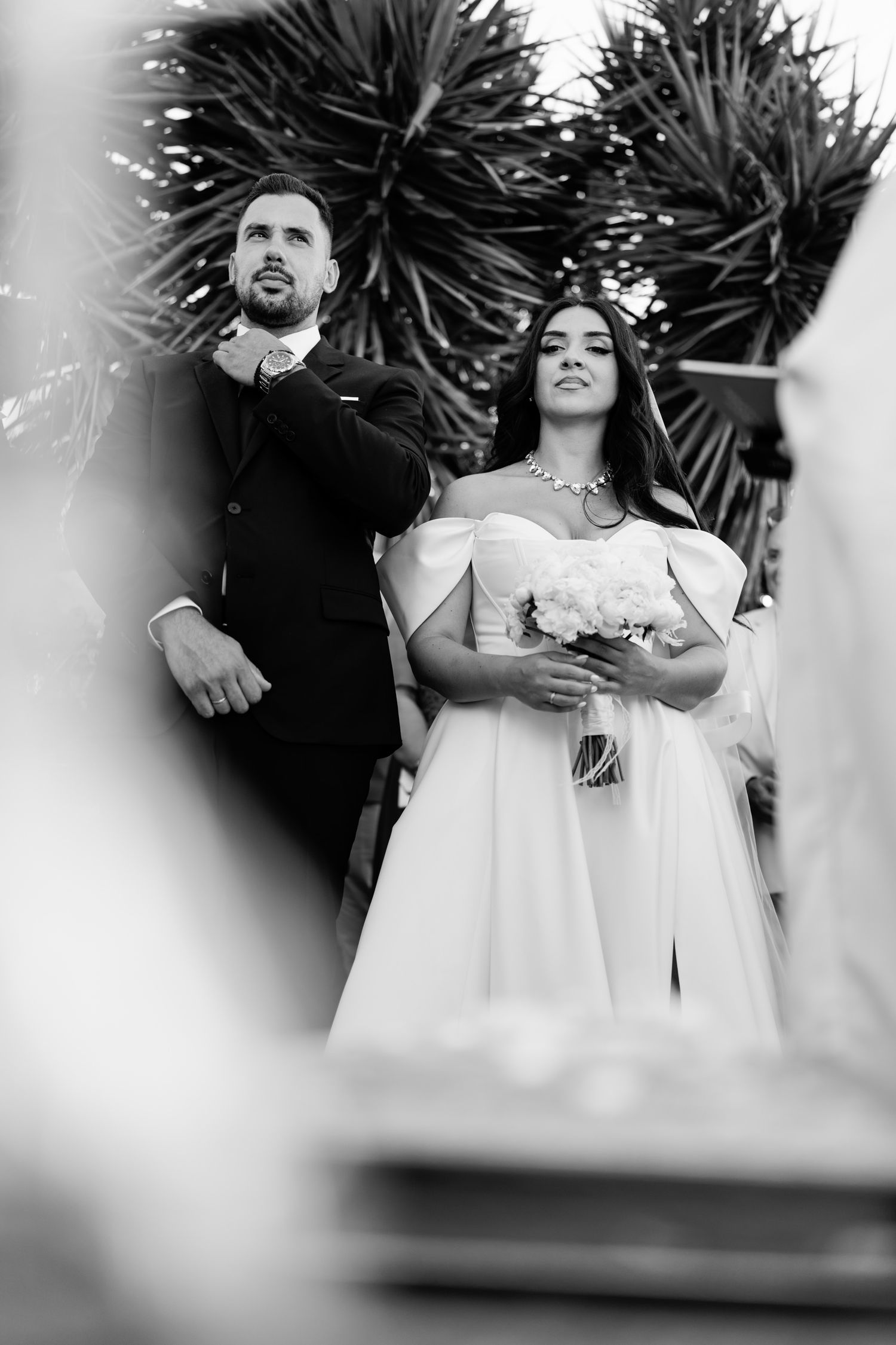 Black and white wedding photo with tropical plants in background.