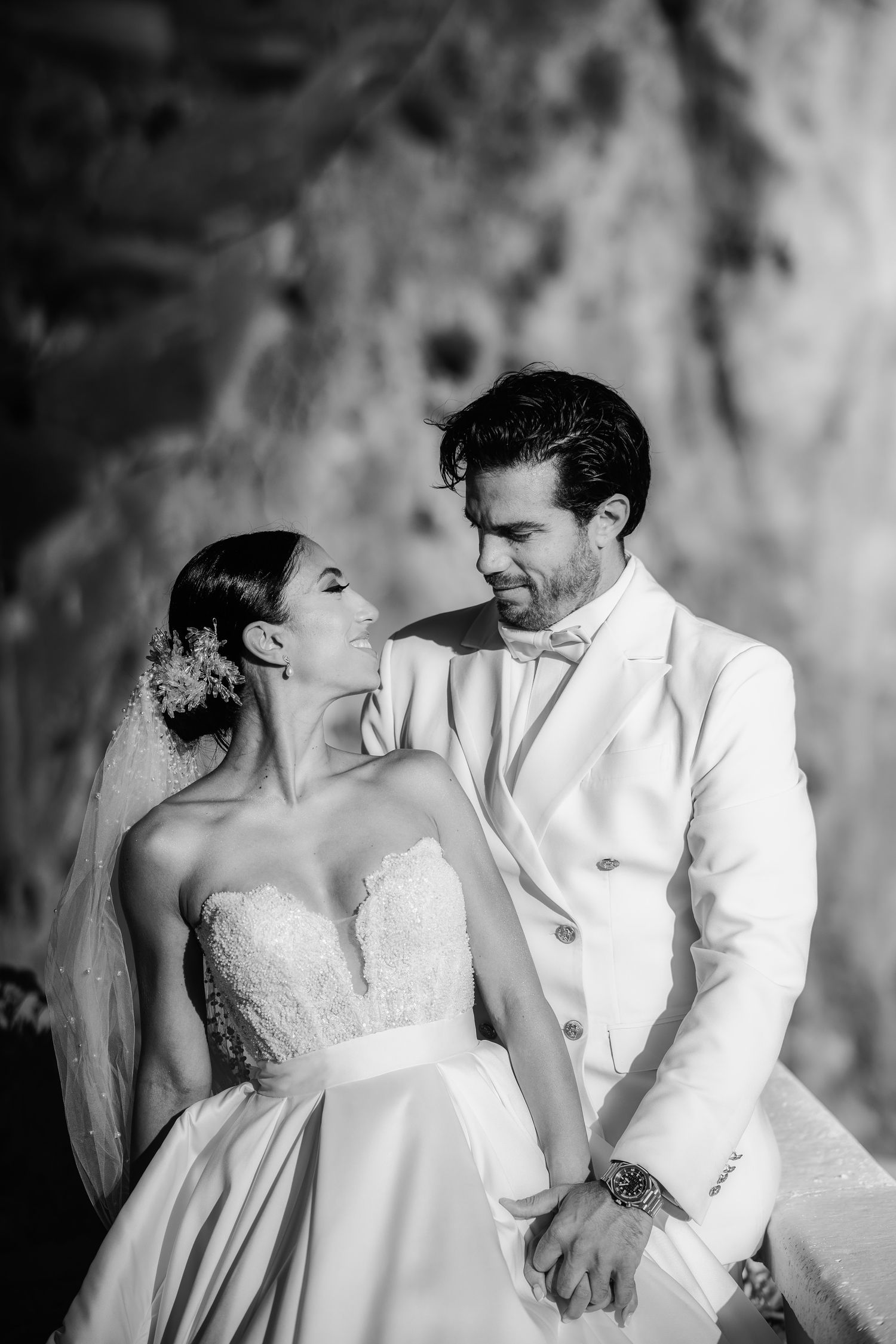 A black and white portrait of newlyweds sharing an intimate moment against a textured wall.