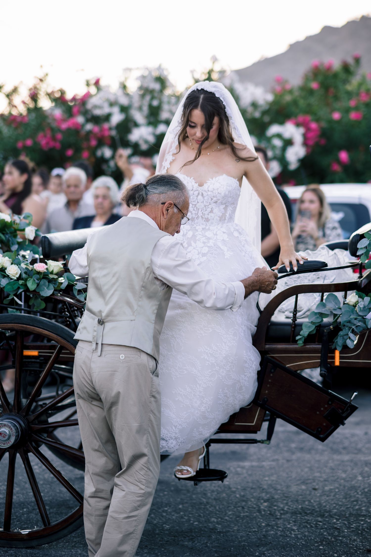 Wedding couple entering horse-drawn carriage surrounded by blooming flowers at dusk.