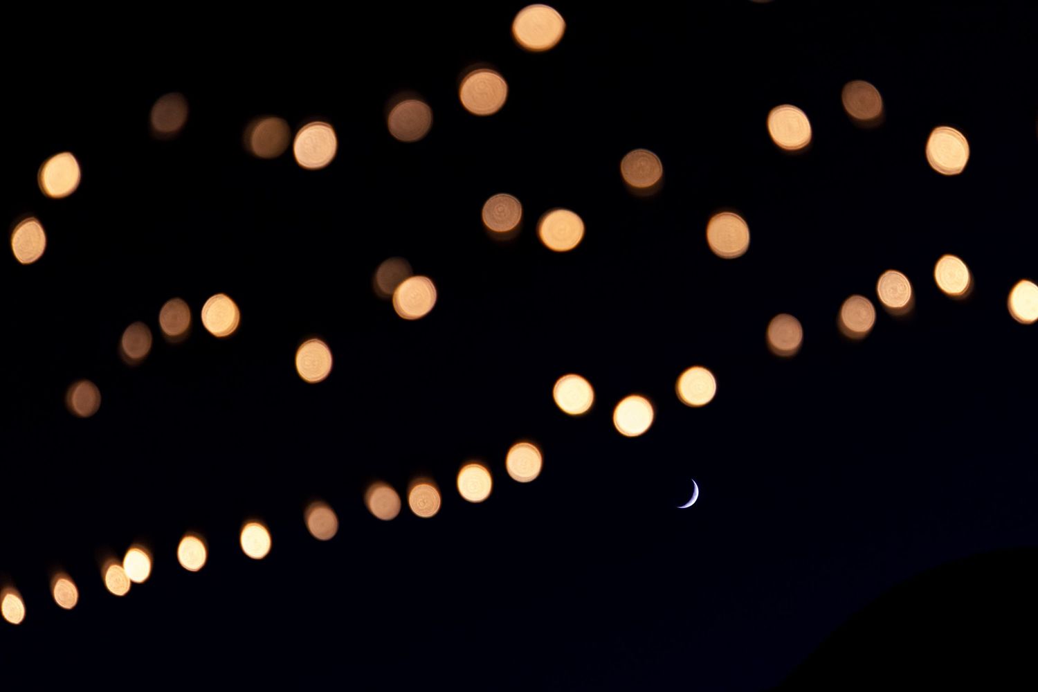 String lights create a magical bokeh effect against the night sky with a crescent moon.