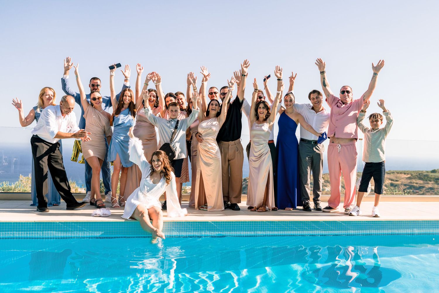 Wedding party celebrating and jumping into a pool with ocean views.