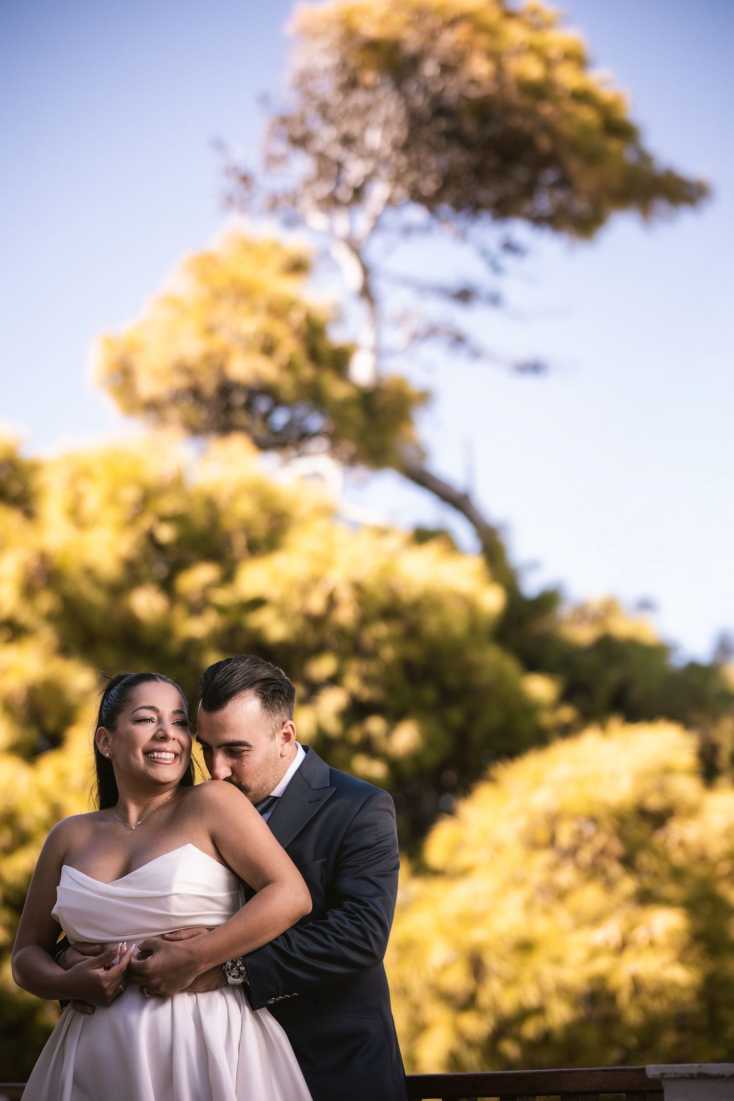 Romantic wedding couple embracing under golden autumn trees in sunlight.
