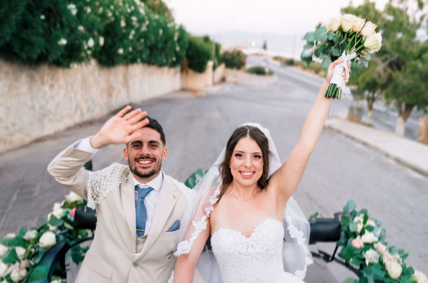 A newlywed couple celebrates joyfully on a street with the bride holding a bouquet.
