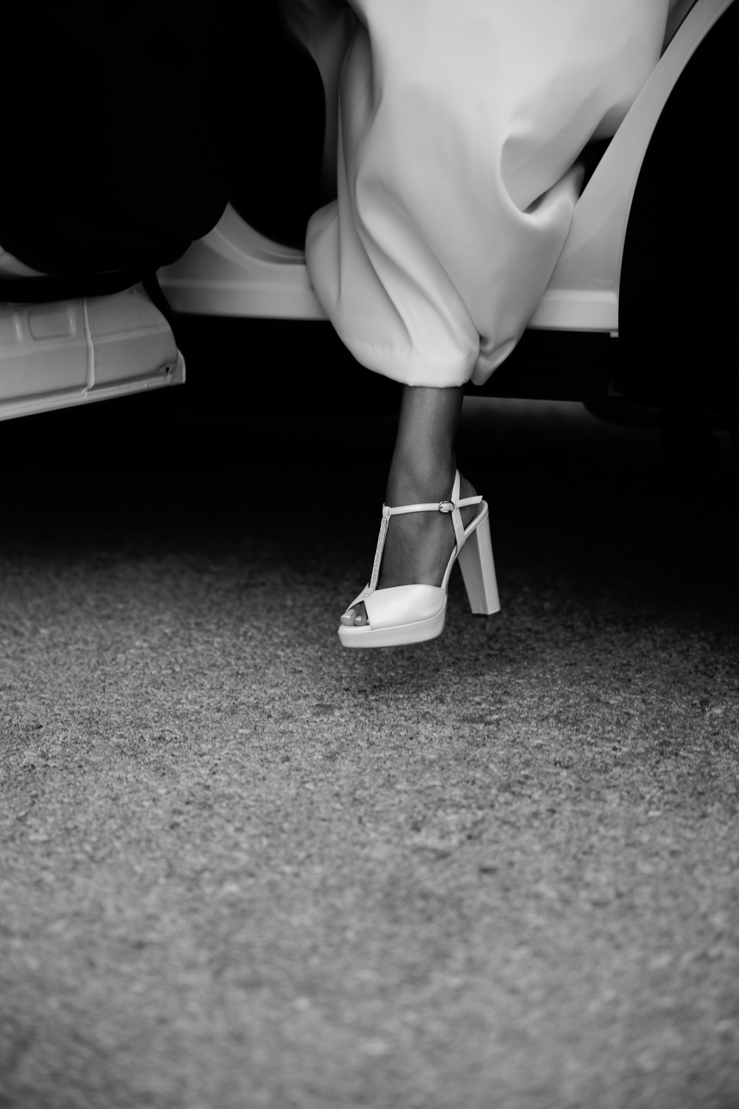 Black and white detail shot of elegant white platform wedding shoe on dark carpet.