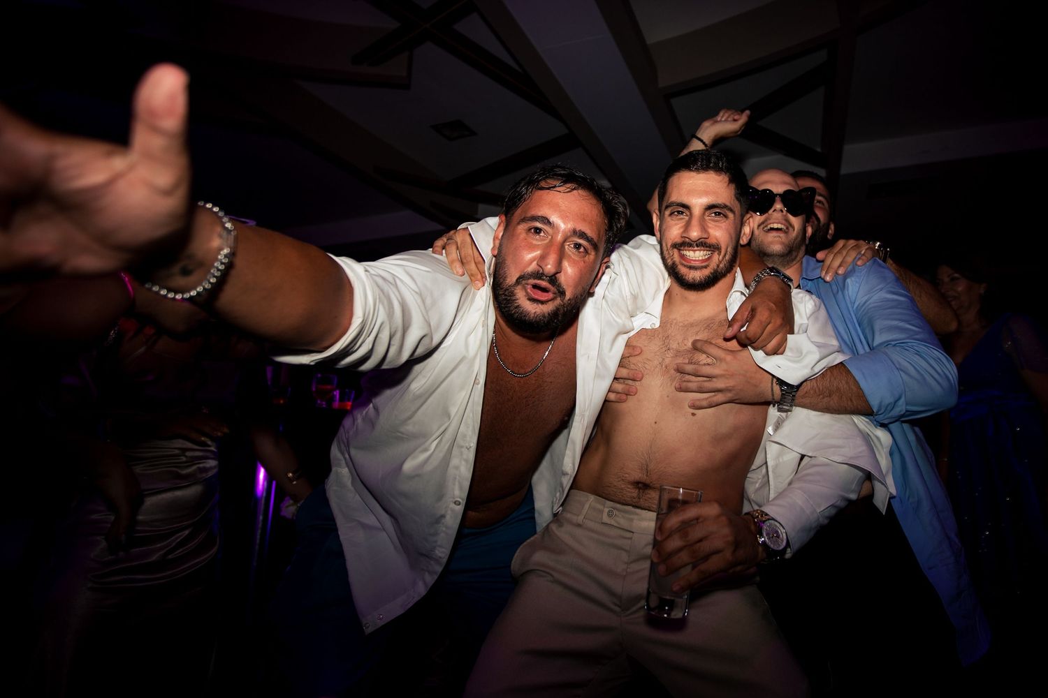 Party guests dance and celebrate energetically in a dark nightclub setting.