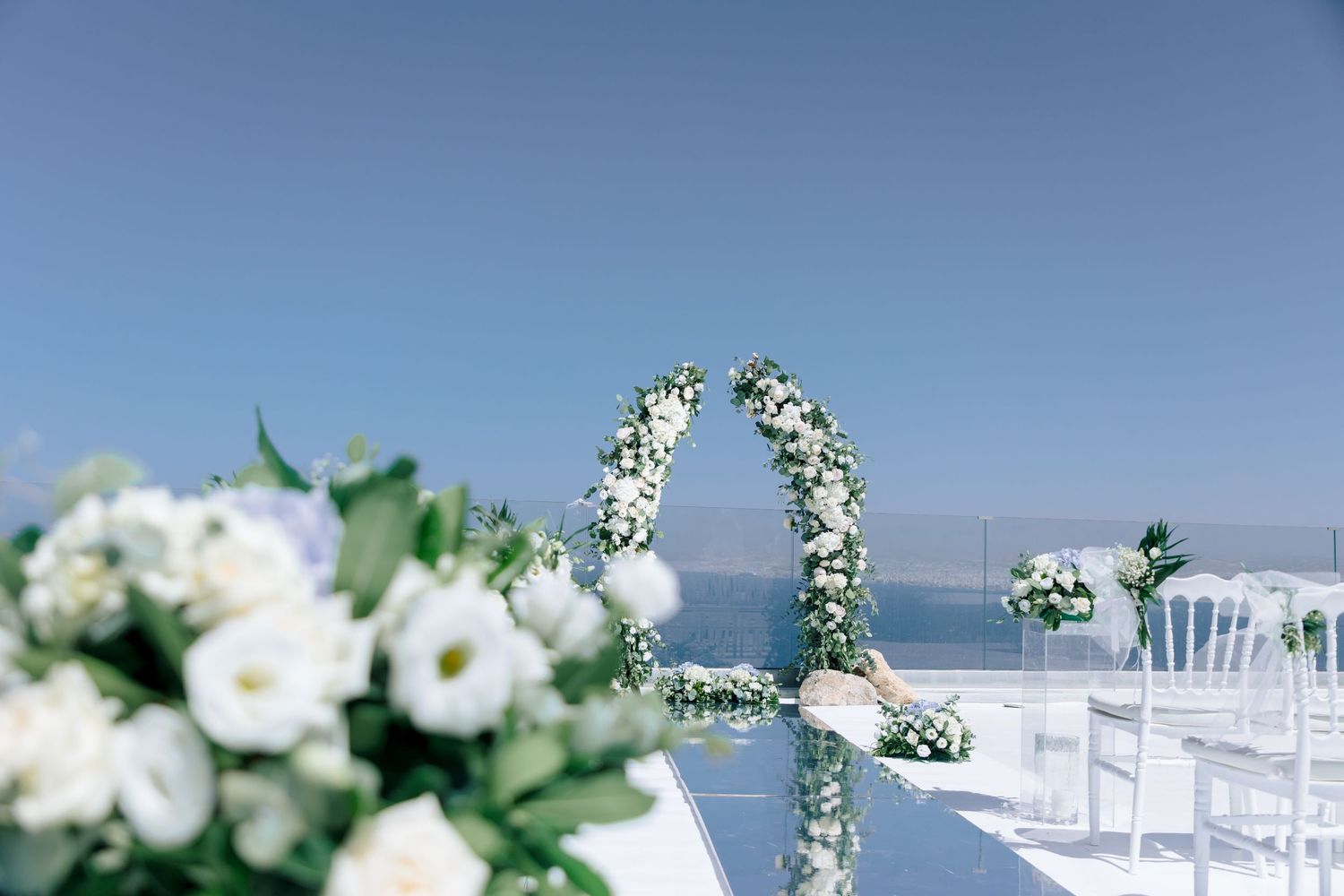 Elegant white floral arrangements and chairs set up for outdoor wedding ceremony with ocean view.