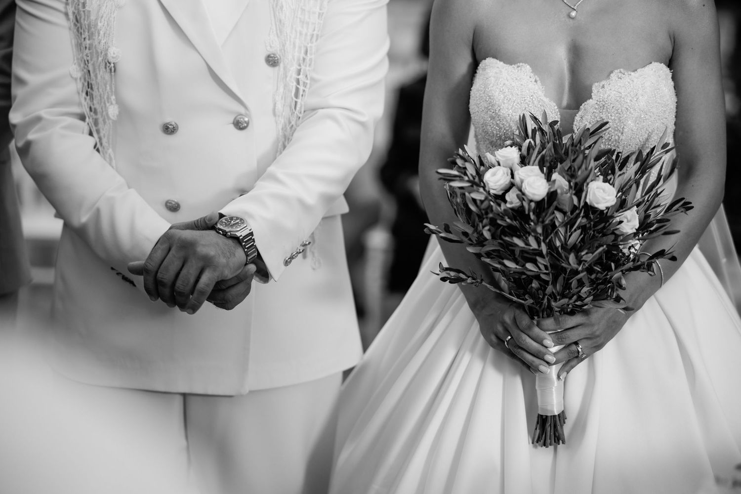 Wedding party members hold elegant bouquets featuring white flowers and greenery against white formal attire.